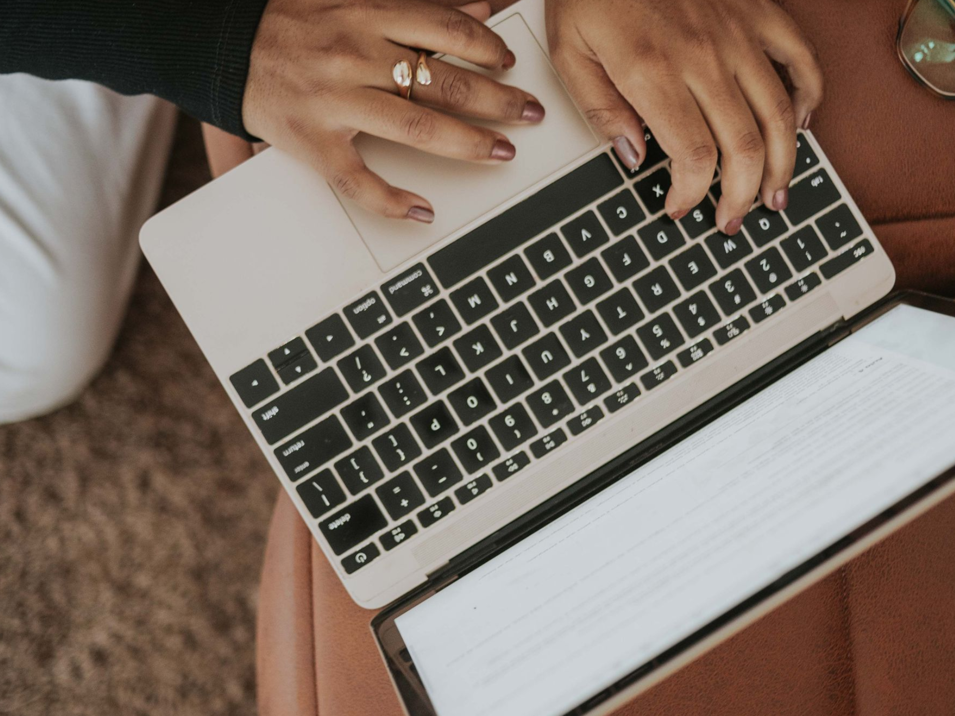 Hands typing on a laptop over a notebook, viewed from above