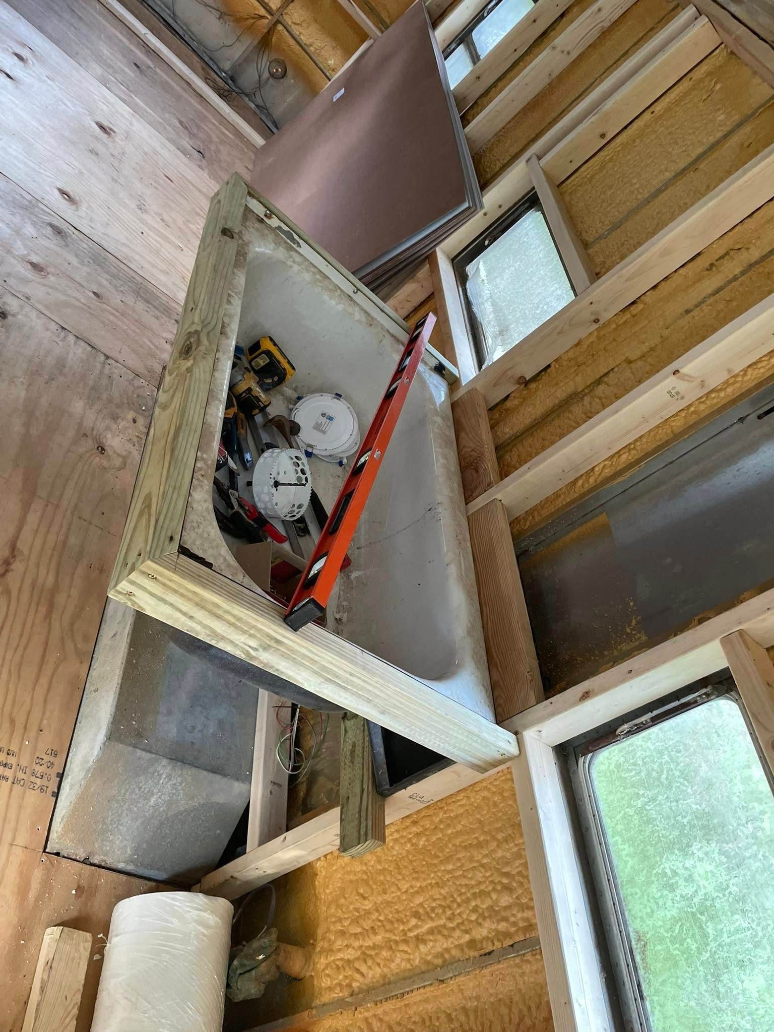 A bathtub installed in a framed wall opening under construction with tools and supplies visible inside.