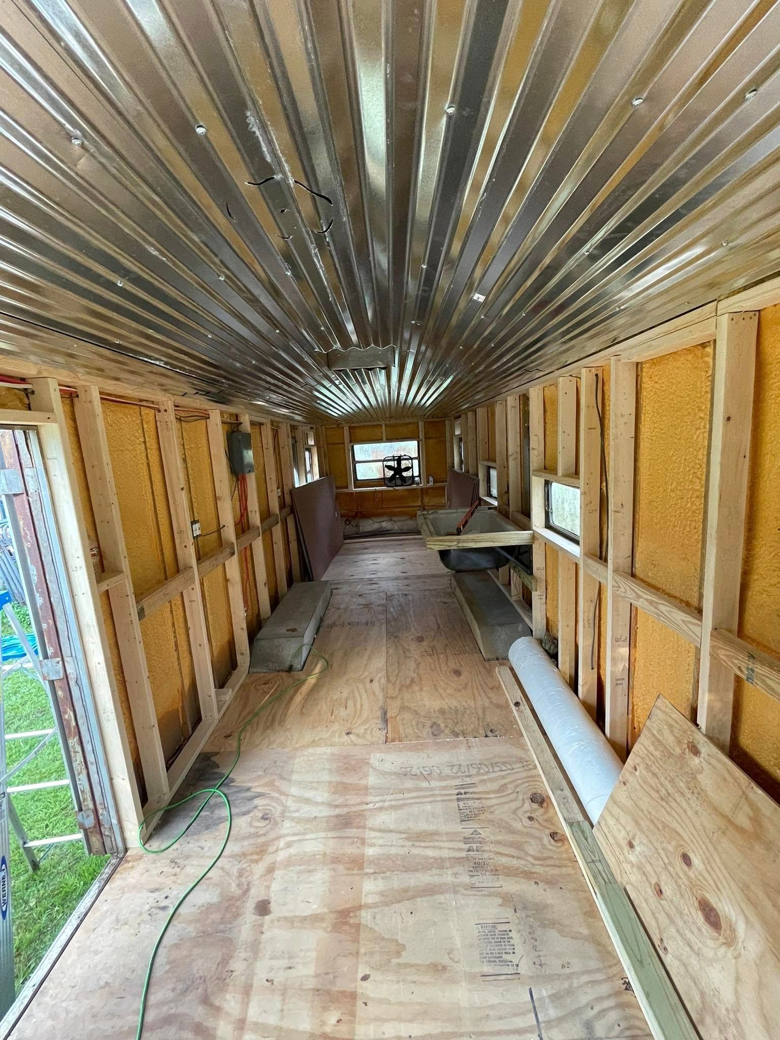 Interior of a bus conversion project with wood-framed walls, insulation, and a corrugated metal ceiling.