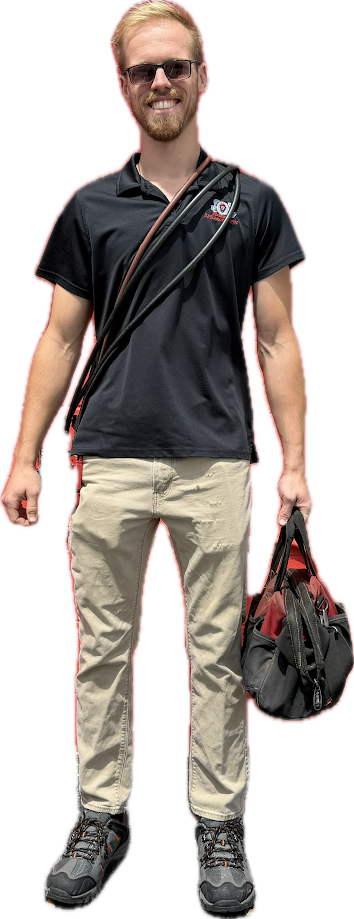 Person standing in black shirt and beige pants, holding a bag, with sunglasses and a crossbody strap