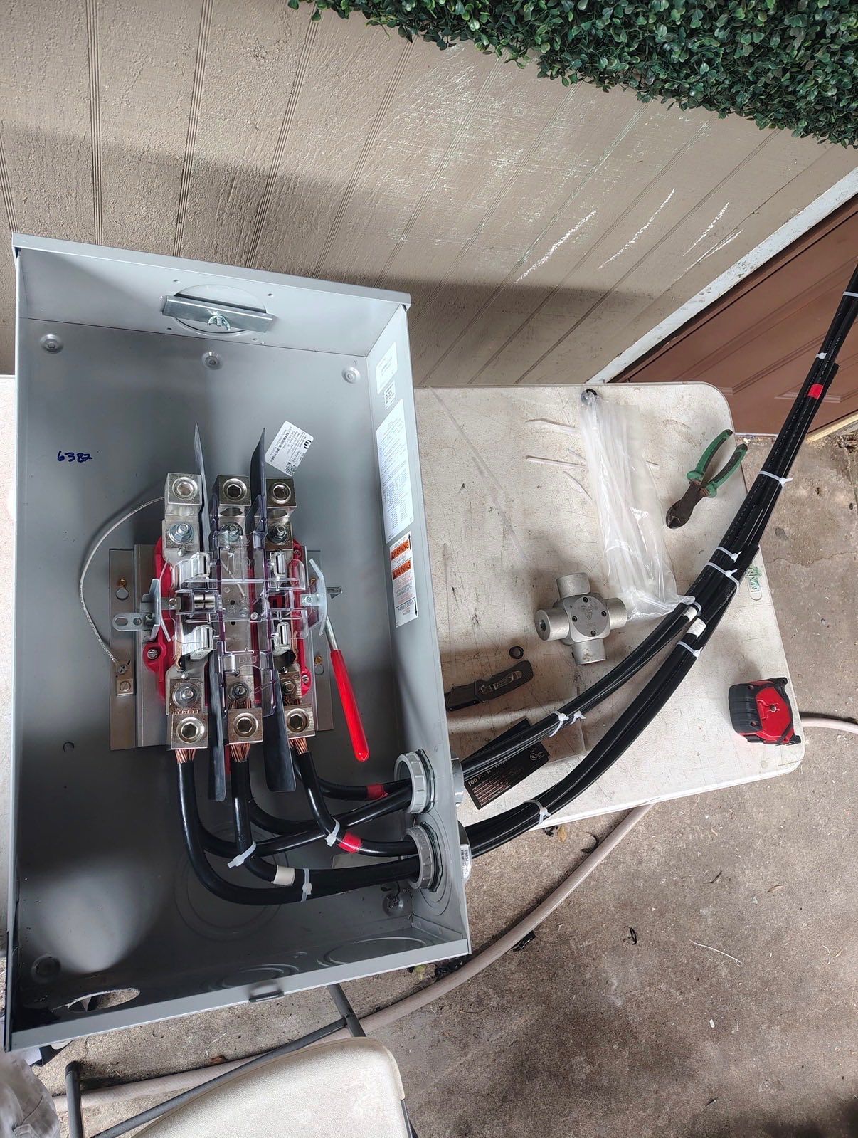 Open metal electrical panel with wiring and relays beside a red-handled cable on a carpeted floor