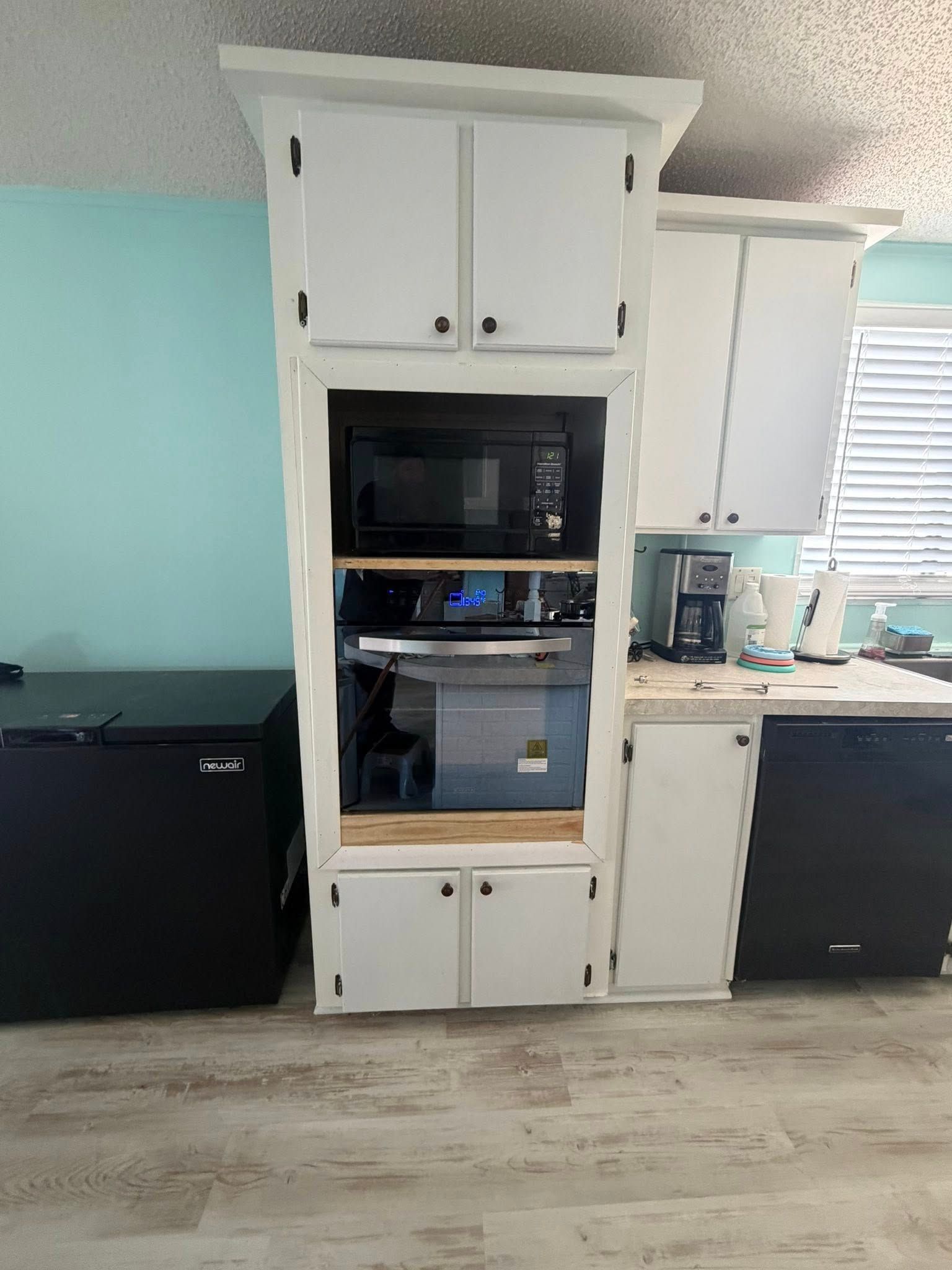Kitchen wall with white cabinets, built-in oven, sink, and black appliances on a light blue wall