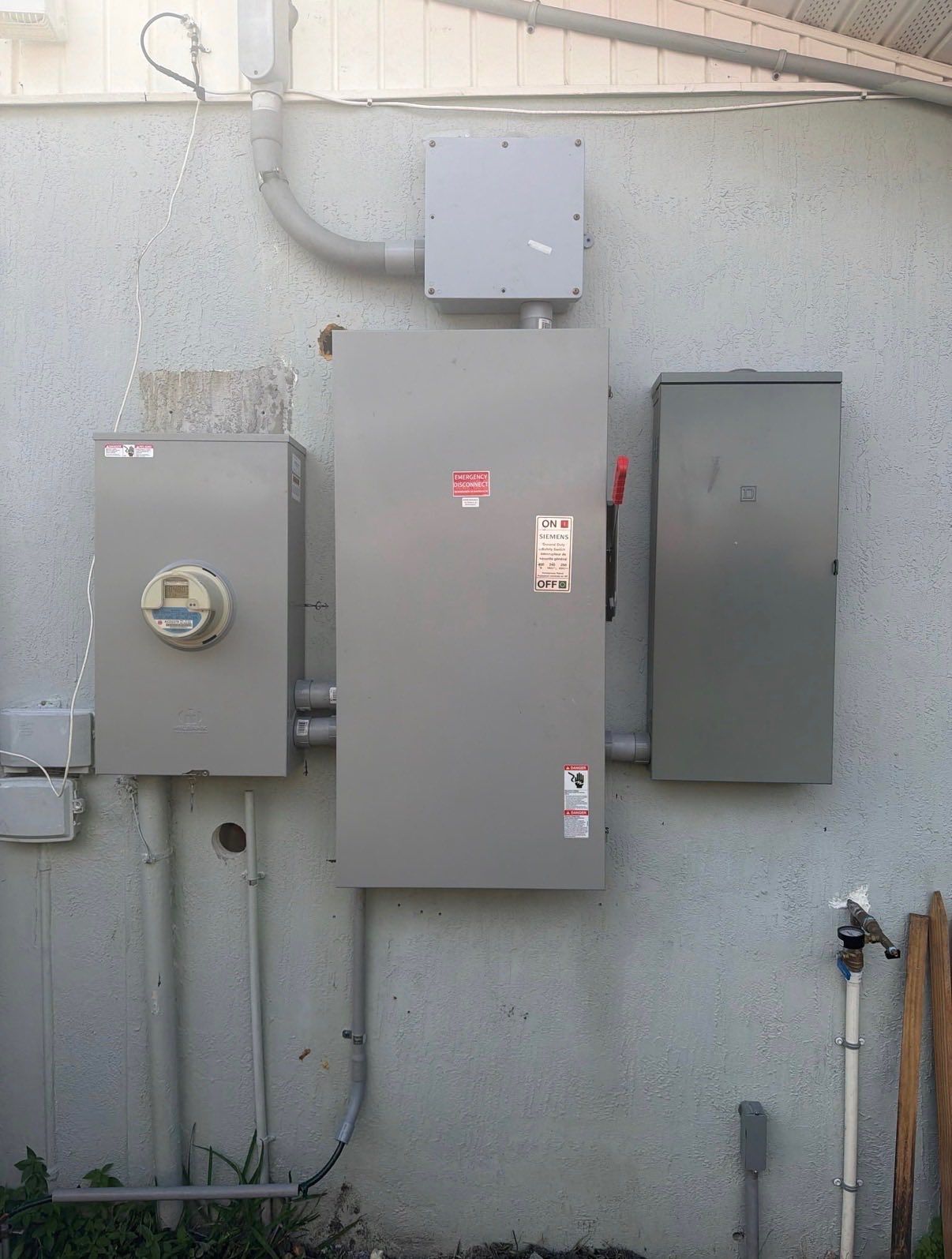 Three gray electrical utility boxes mounted on an exterior stucco wall.