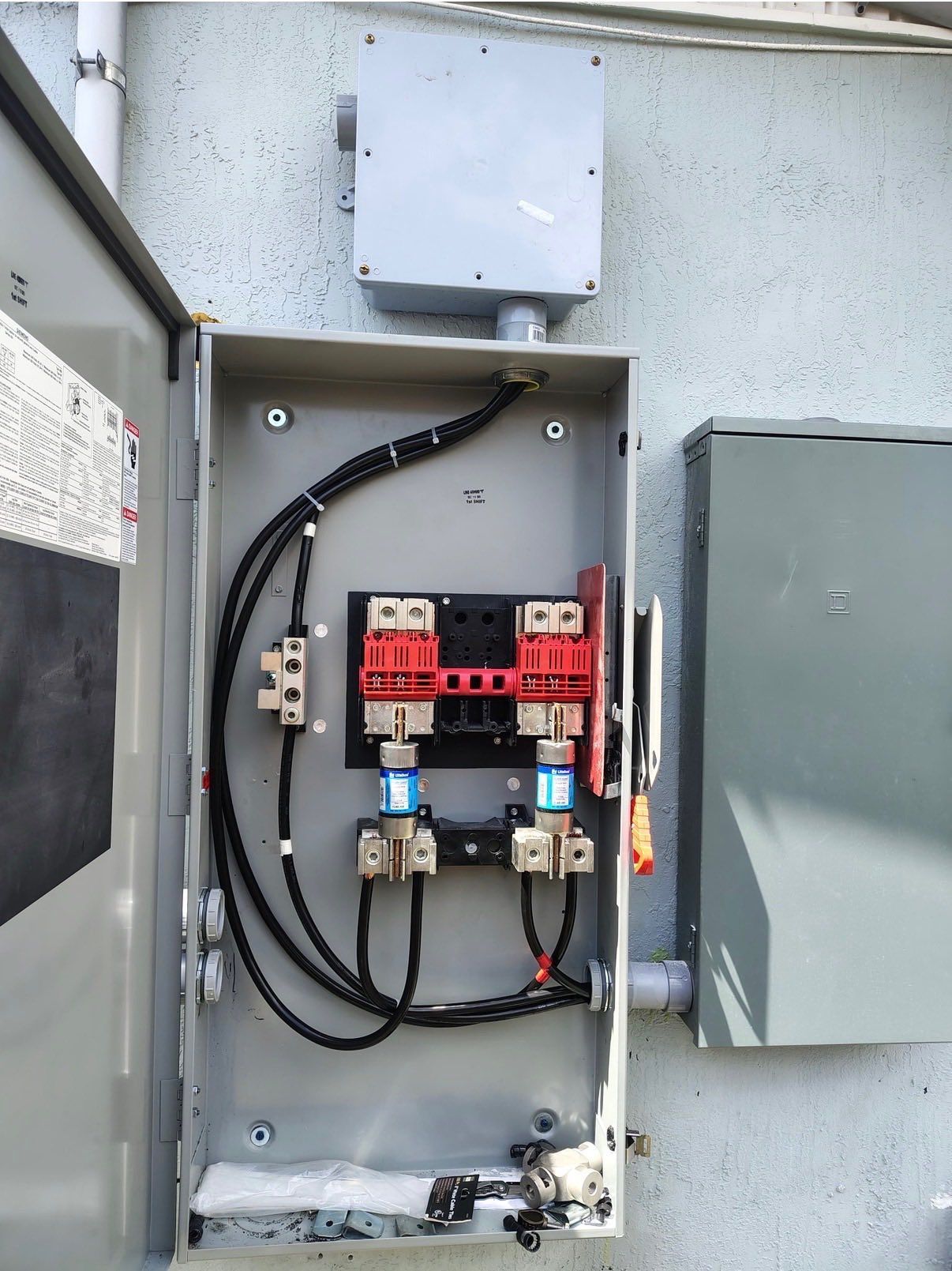 Open electrical service panel with breakers and wiring mounted on an exterior wall.