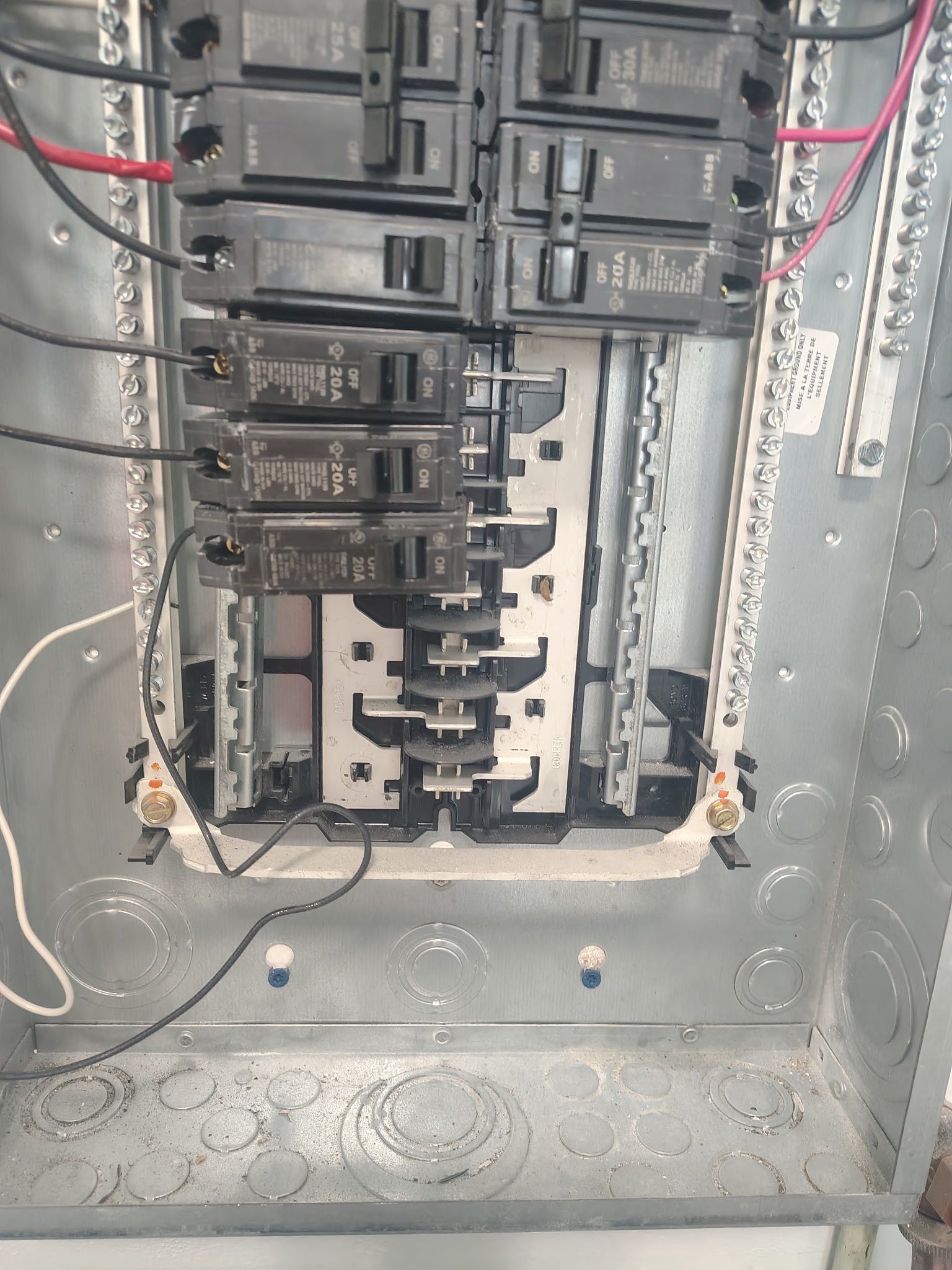Open electrical breaker panel with exposed wiring and multiple black circuit breakers