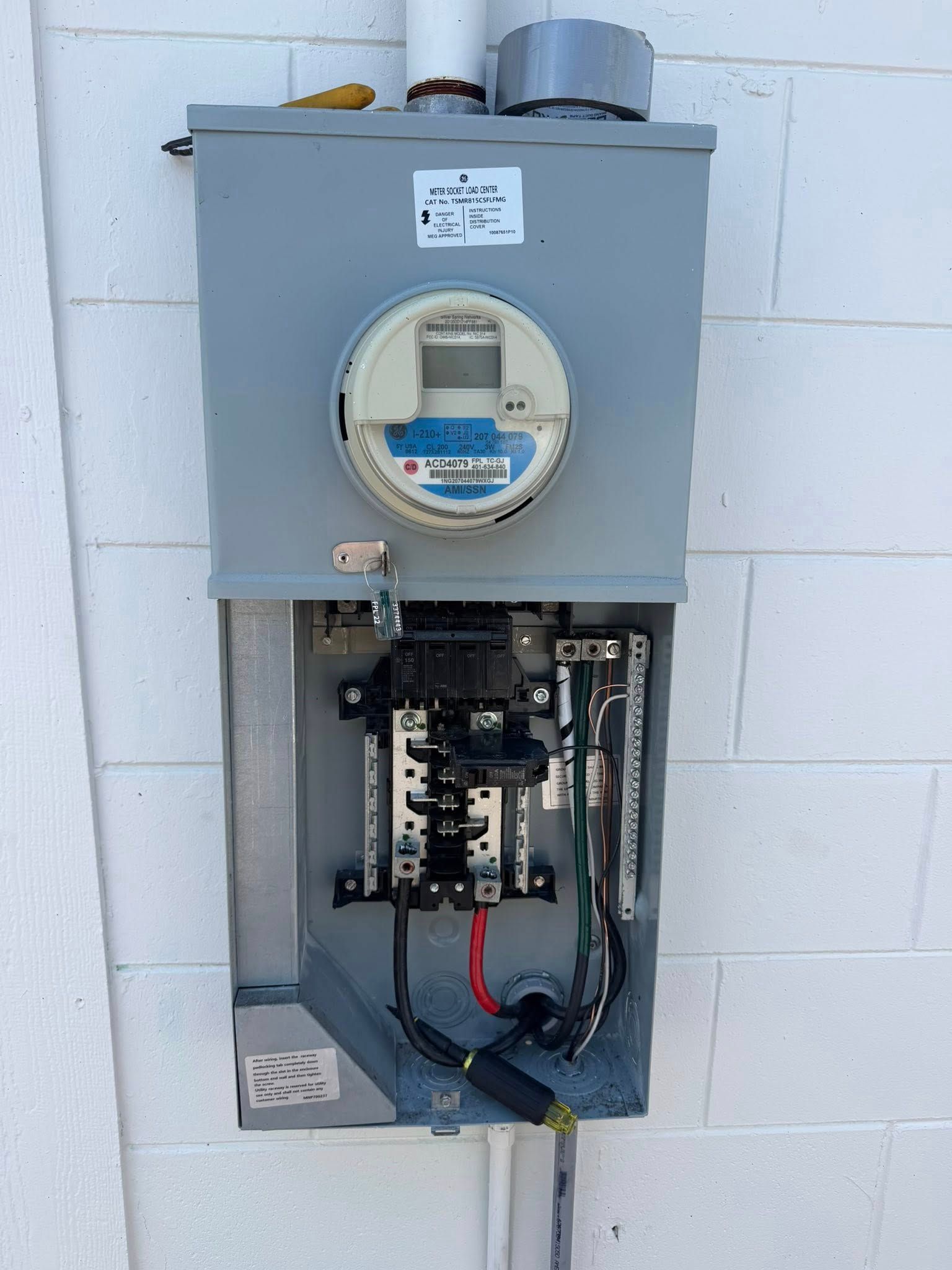 Electric meter and open electrical service panel mounted on a white block wall