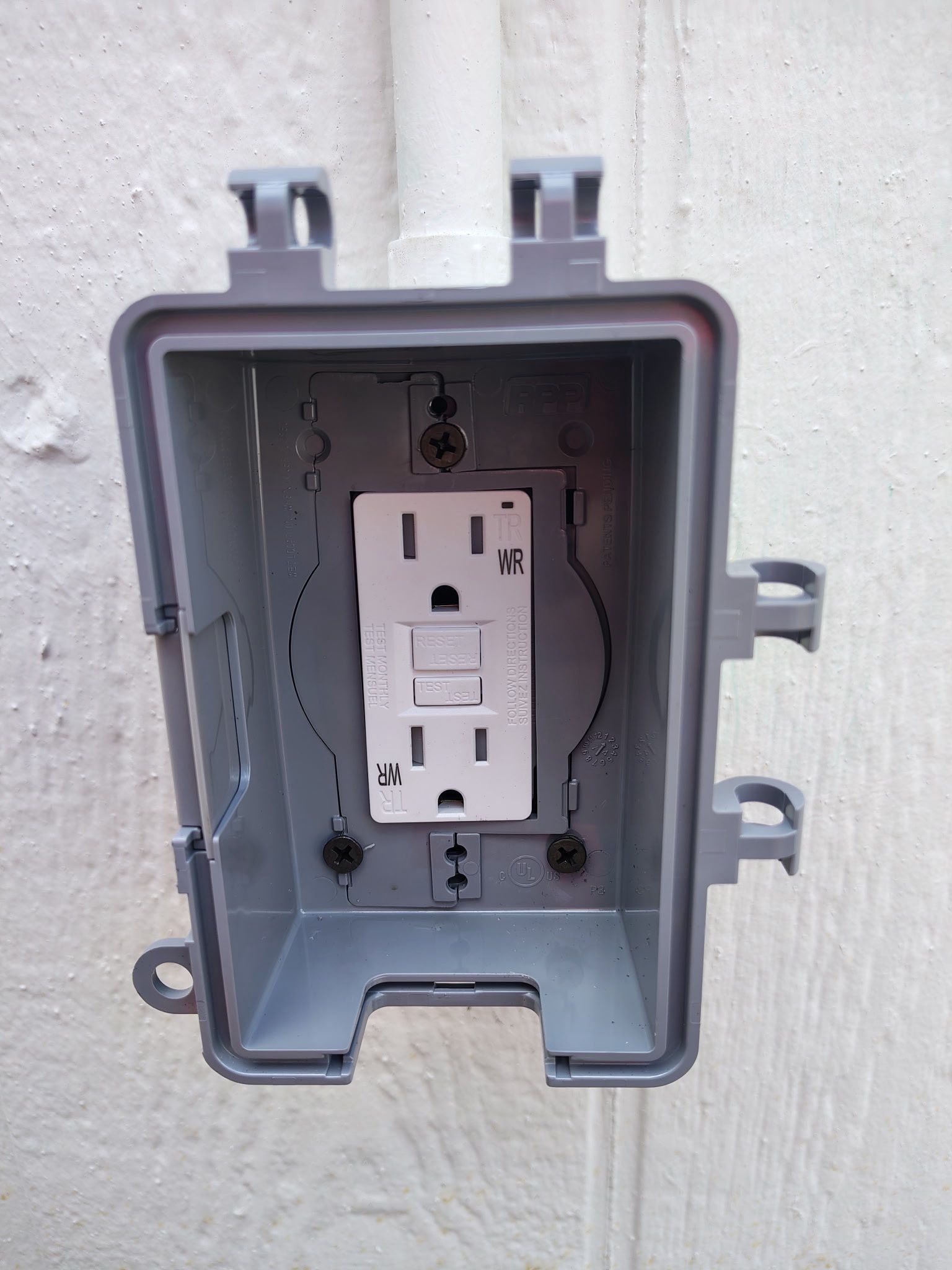 Gray outdoor electrical box with a white GFCI outlet mounted inside on a wall.
