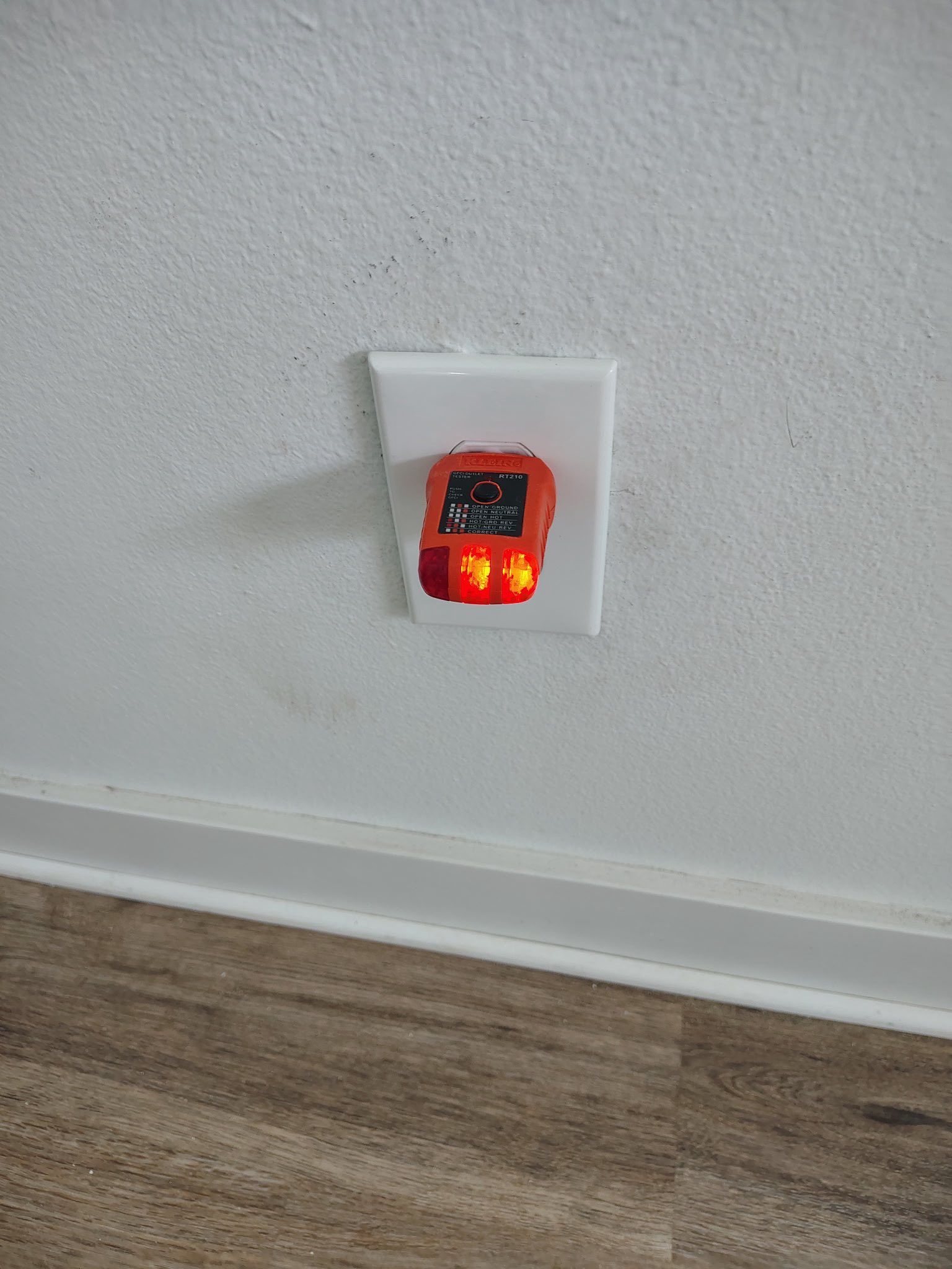 Small red night light plugged into a white wall outlet above a wooden floor.