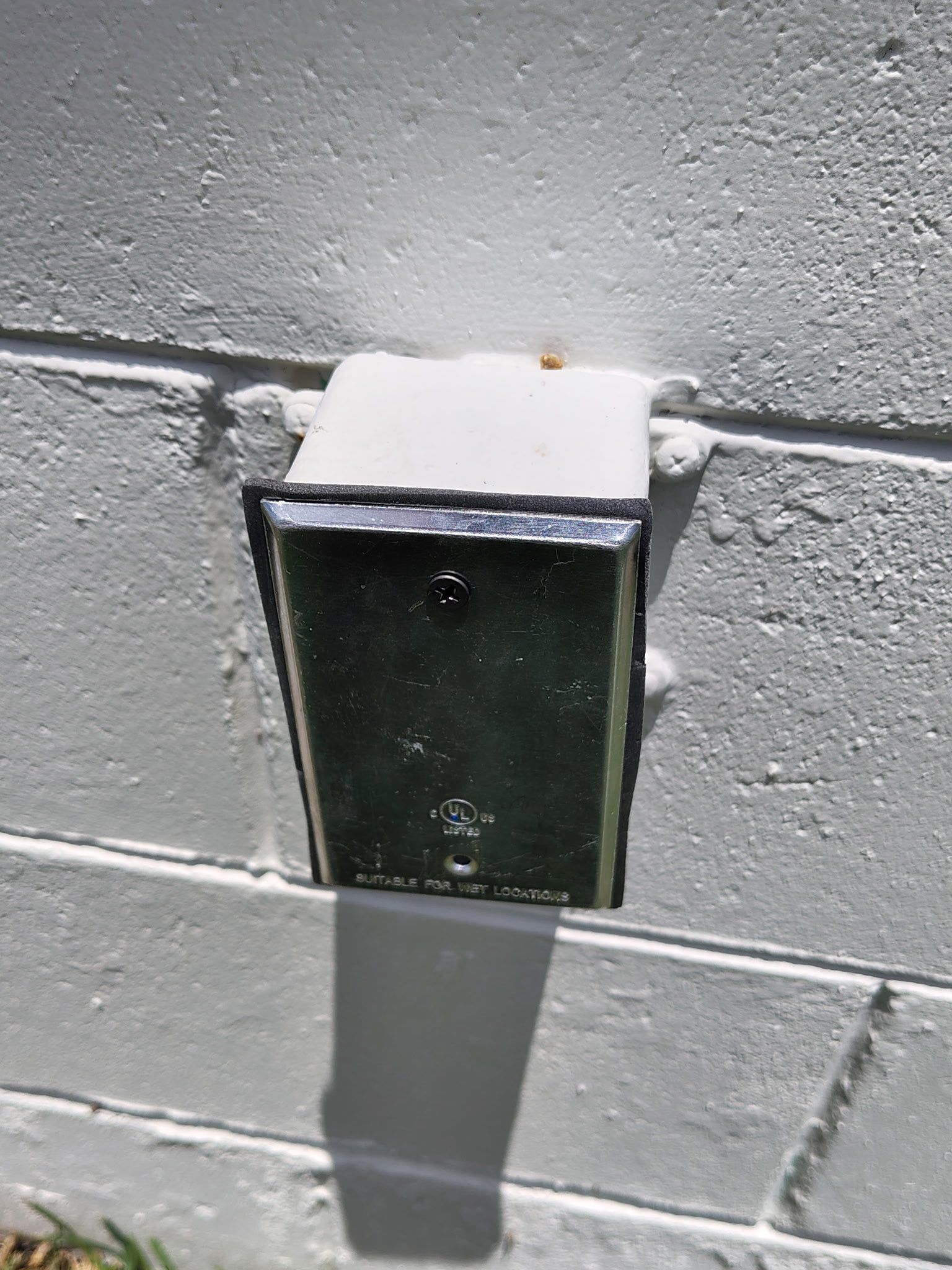 Wall-mounted outdoor light fixture casting a long shadow on a cinder block wall.