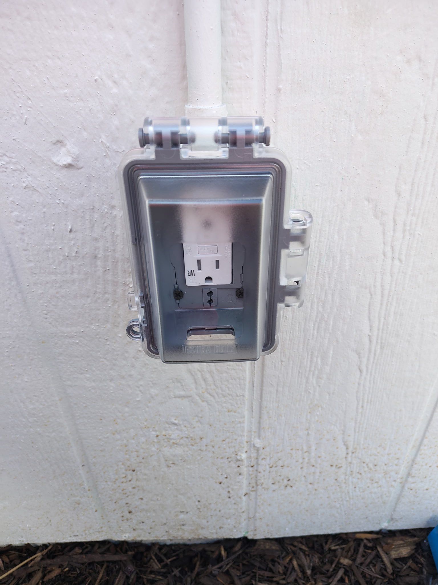 Outdoor electrical outlet in a weatherproof metal box mounted on a wall.