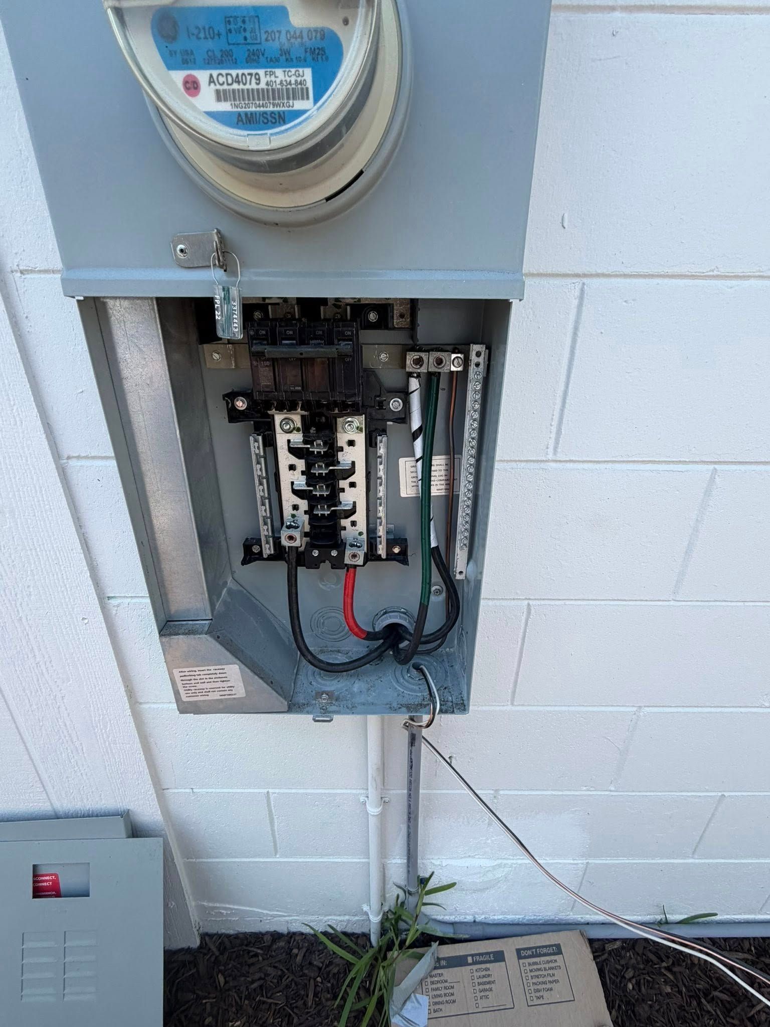 Open electrical meter panel with exposed wiring mounted on a cinderblock wall
