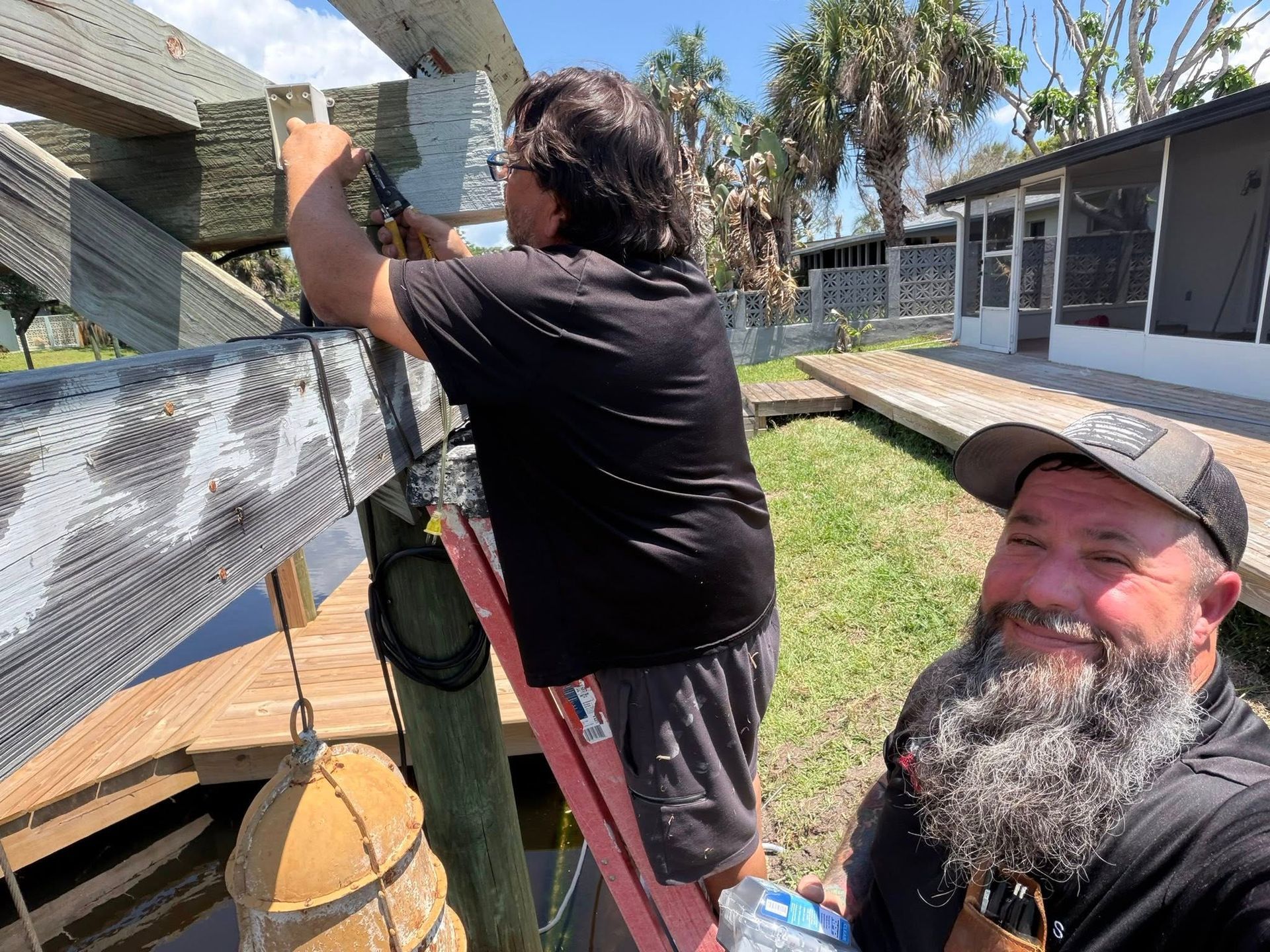 Two men working on a rooftop, one holding a tool near a vent on a sunny day