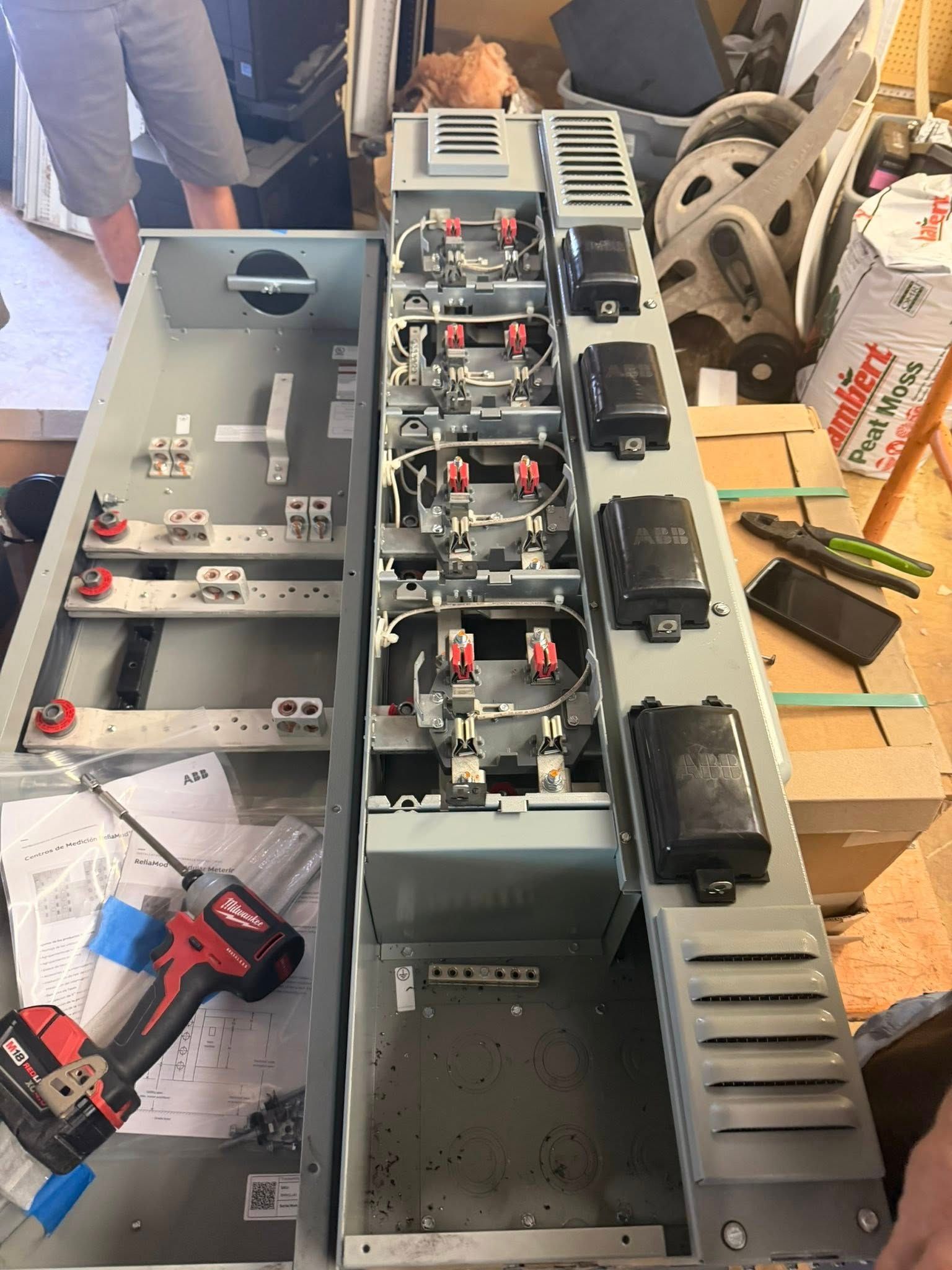 Open circuit breaker panel on a workbench with a red power drill nearby.