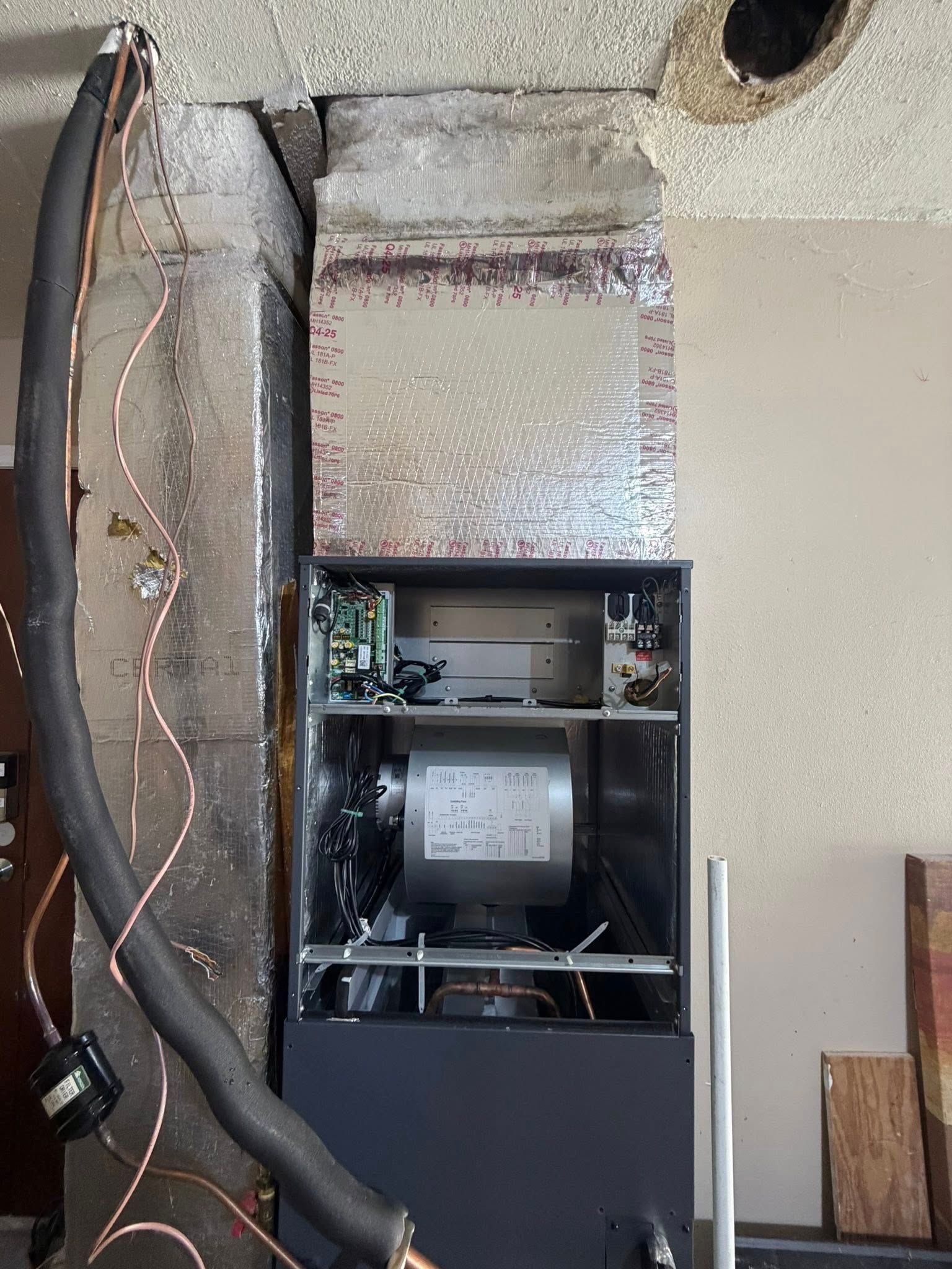 Open wall with exposed ducting and a mounted HVAC furnace unit inside a utility closet.
