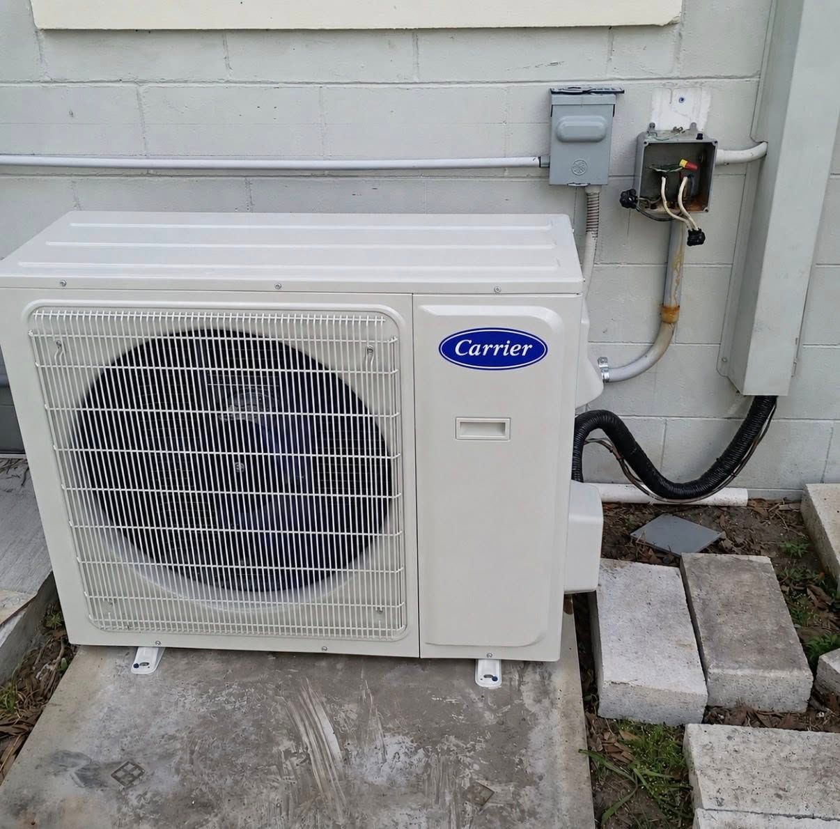 Outdoor Carrier air conditioner unit beside a house wall with electrical disconnect and concrete blocks nearby