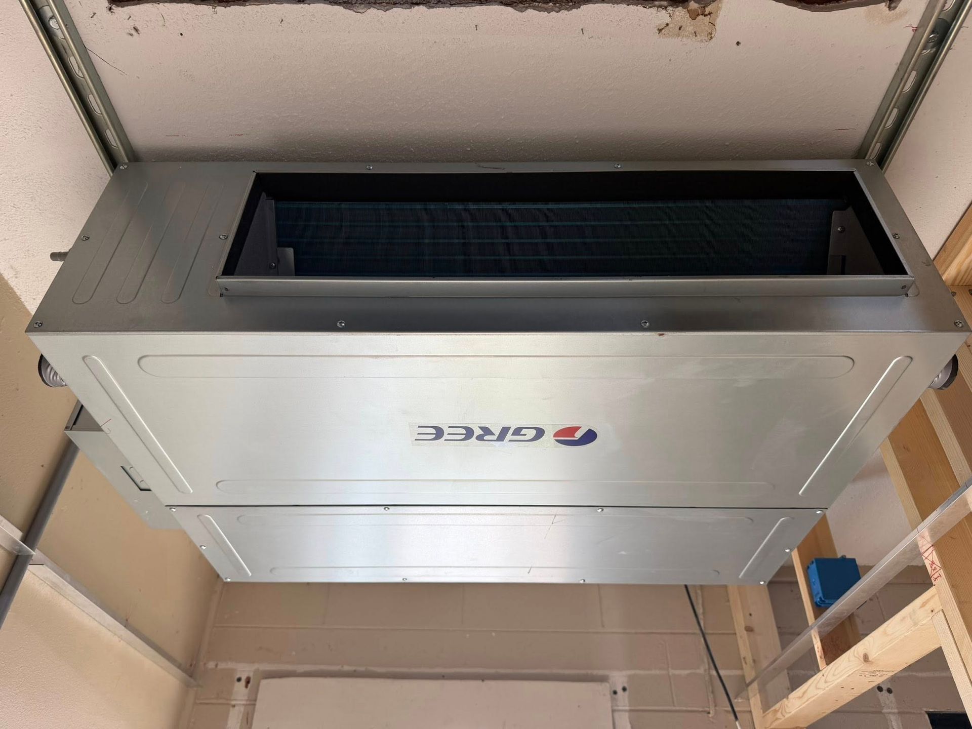 Ceiling-mounted rectangular HVAC unit in a utility room with exposed framing and insulation.