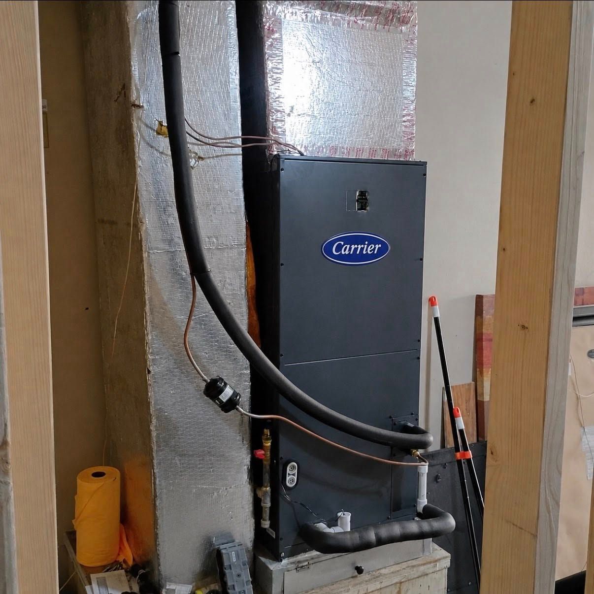 Carrier furnace with black ductwork in a utility closet, between wooden studs and foil insulation.