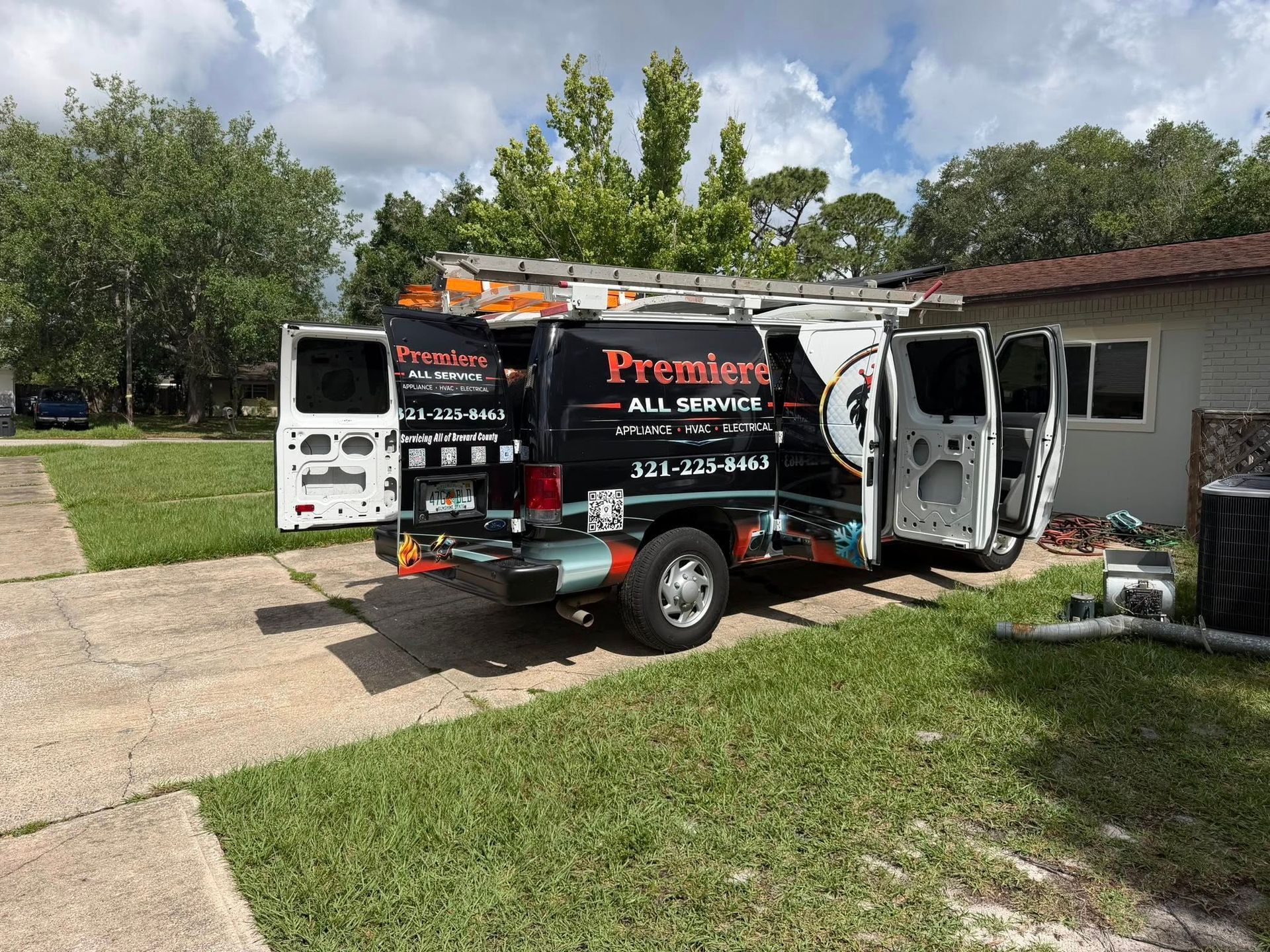Black Premier plumbing van parked in a driveway with side doors open, outside a house.