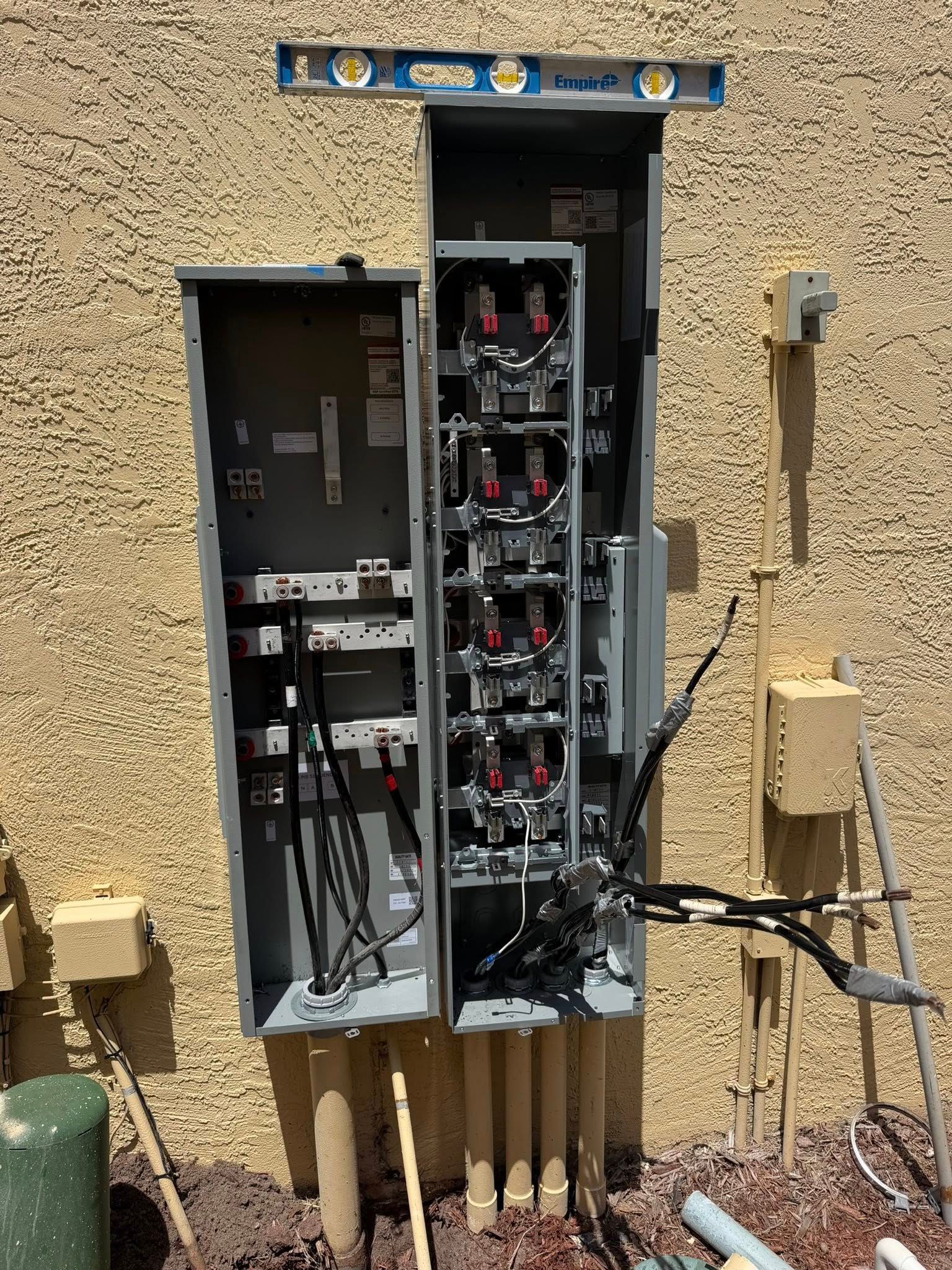Open electrical panels mounted on a stucco wall with exposed wiring and circuit components.