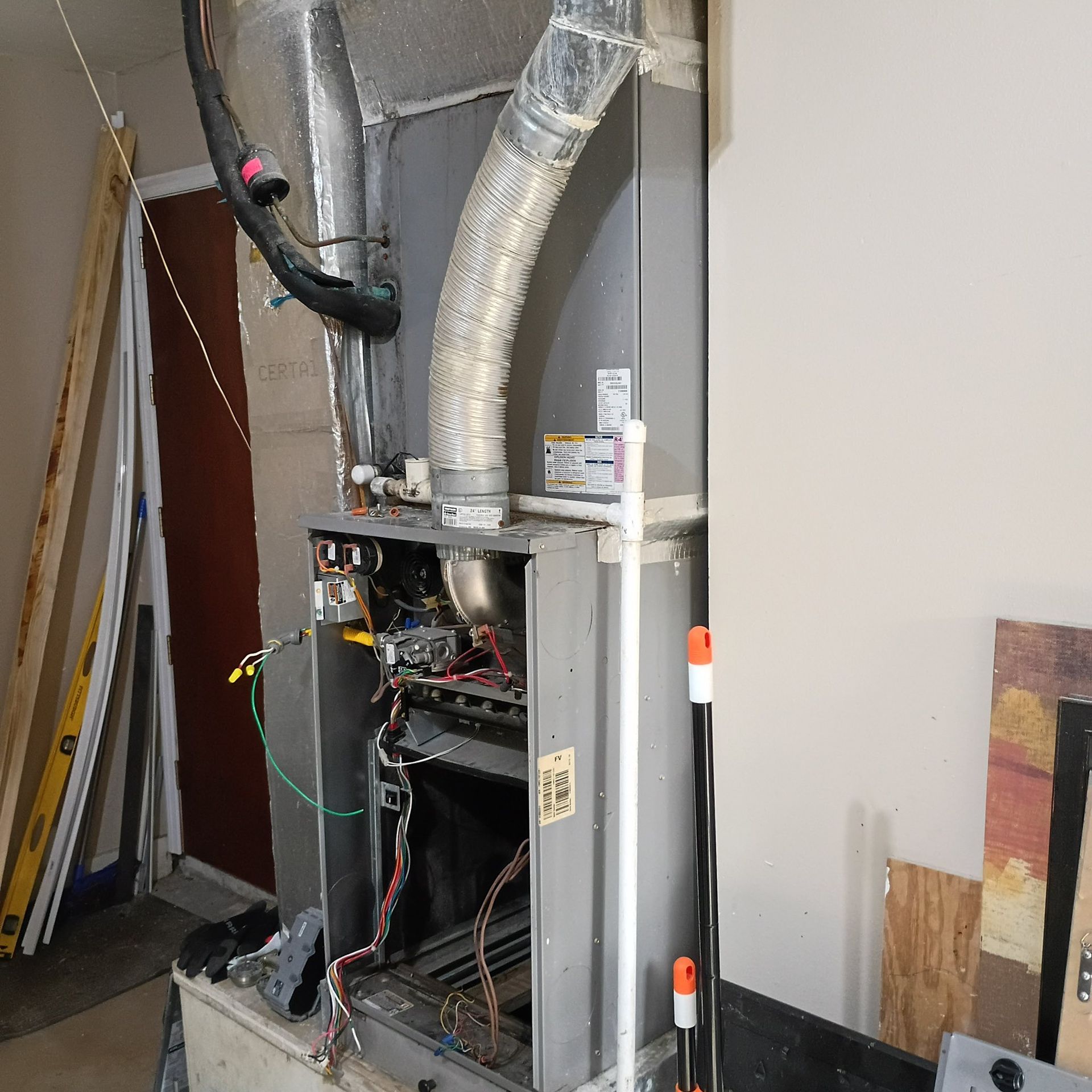 Open furnace cabinet with exposed wiring and ductwork in a utility room during repair work