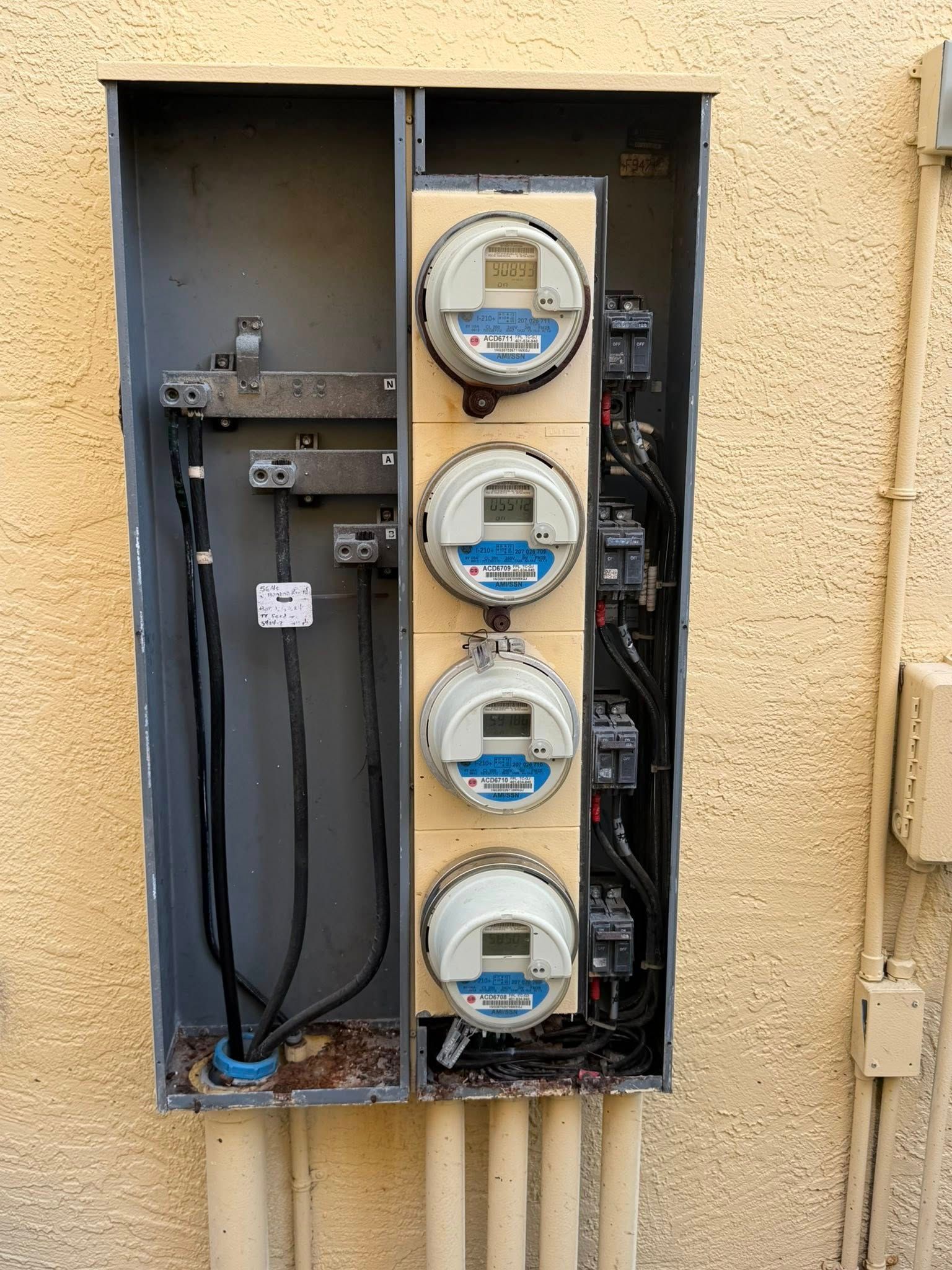 Open electrical meter panel mounted on a beige exterior wall.