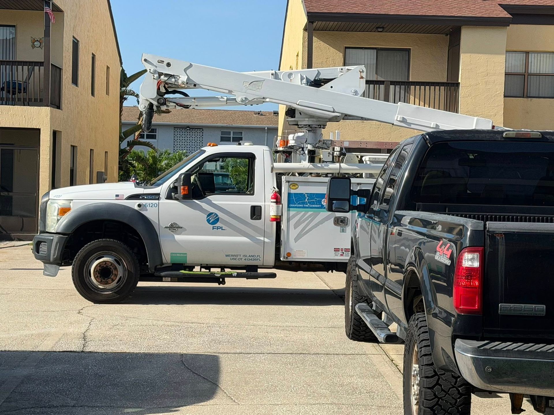 Utility truck with a raised boom parked between buildings, partly blocked by a black SUV.