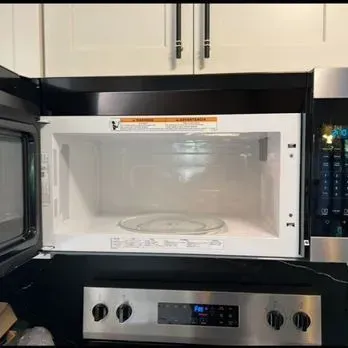 Open microwave in white kitchen cabinets above a stainless steel stove control panel