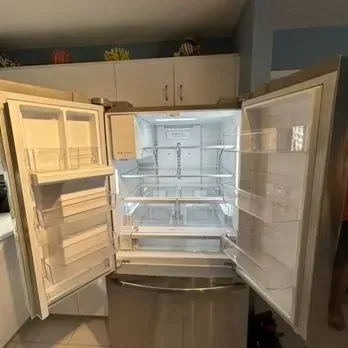Open refrigerator with empty shelves and bright interior light in a kitchen.