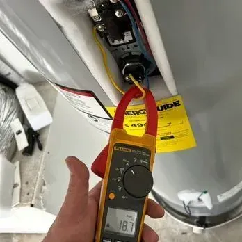 Multimeter testing wiring inside a white appliance, with red and black probes connected to a circuit board