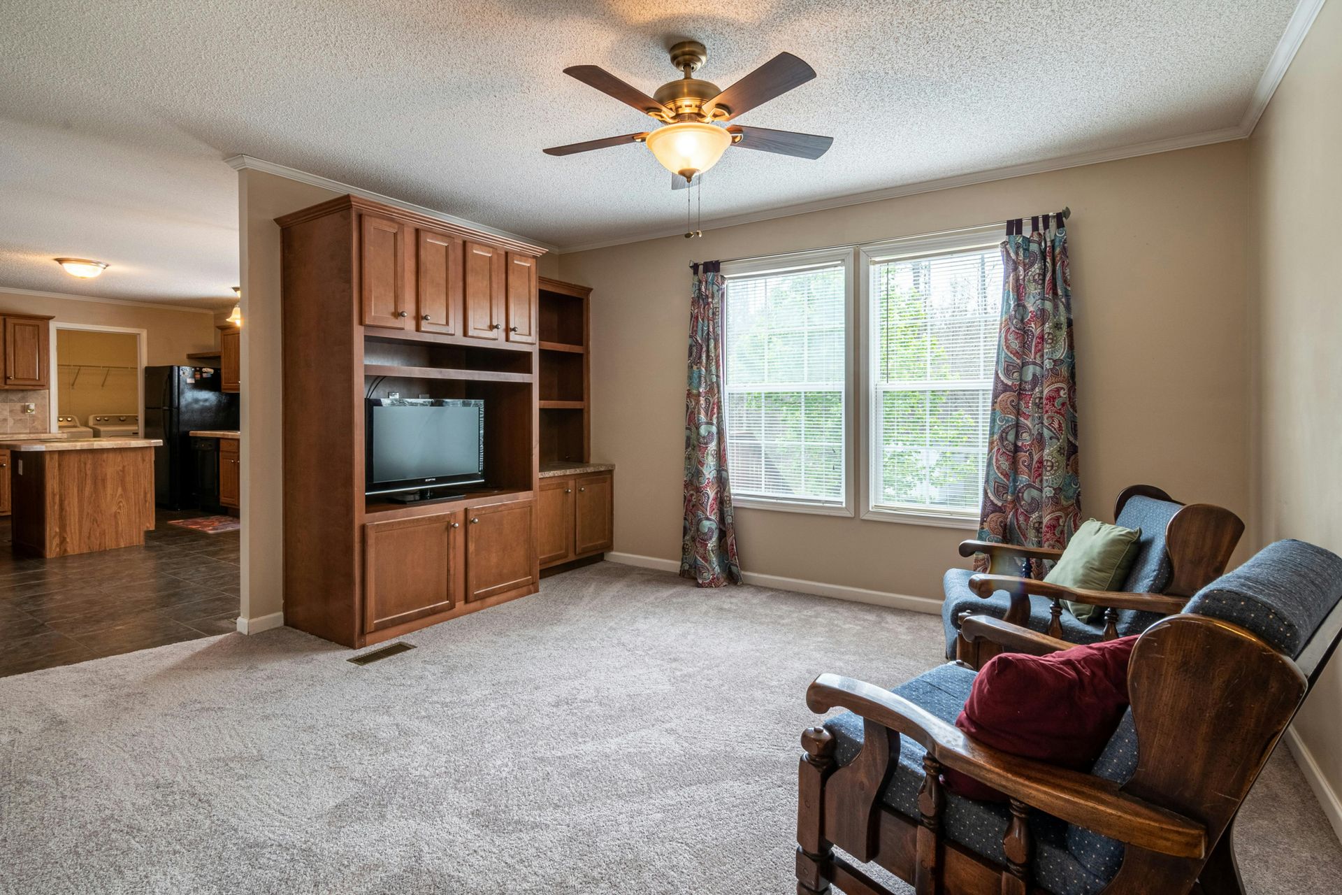 Living room with wood entertainment center, beige carpet, window seats, and two wooden chairs by a bright window