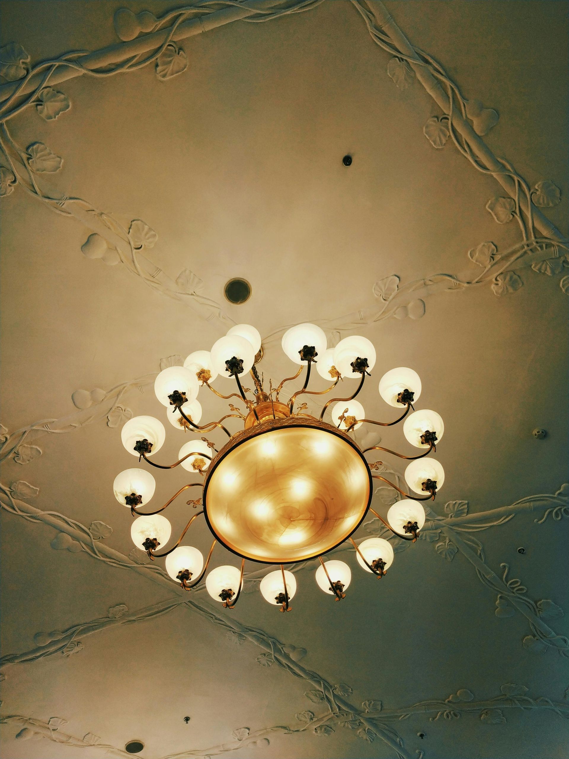 Ornate gold ceiling chandelier with white glass shades on a beige patterned ceiling
