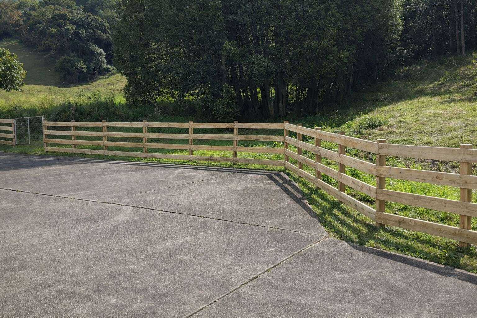 Concrete Driveway Beside a Wooden Fence Overlooking a Grassy Hillside and Trees — Frontline Fences in Kingscliff, NSW