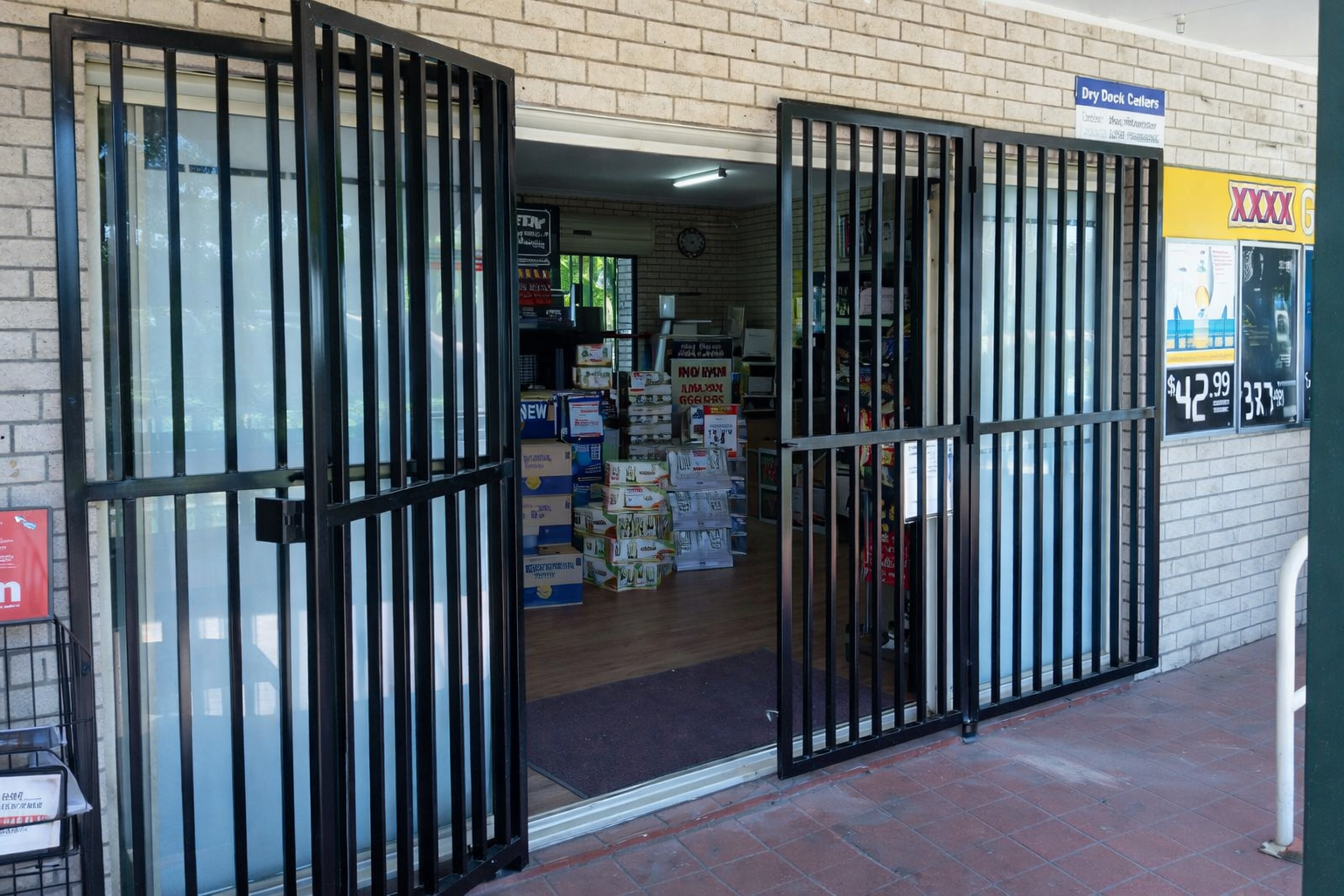 Open storefront with black metal security gates and stacked goods inside a brick building.