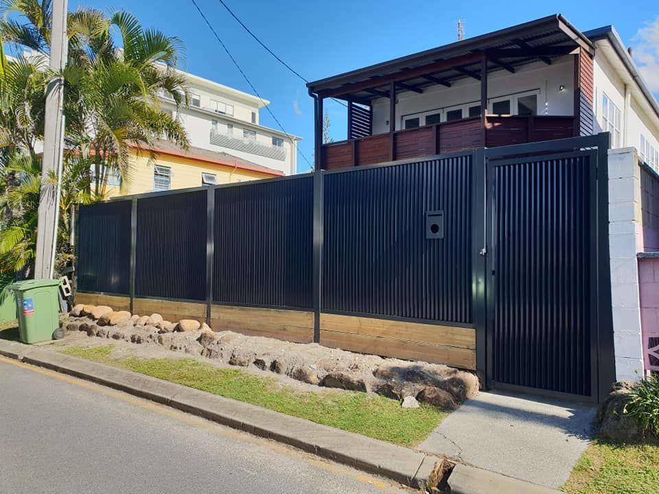 Modern two-story house behind a tall black metal fence along a sunny residential street