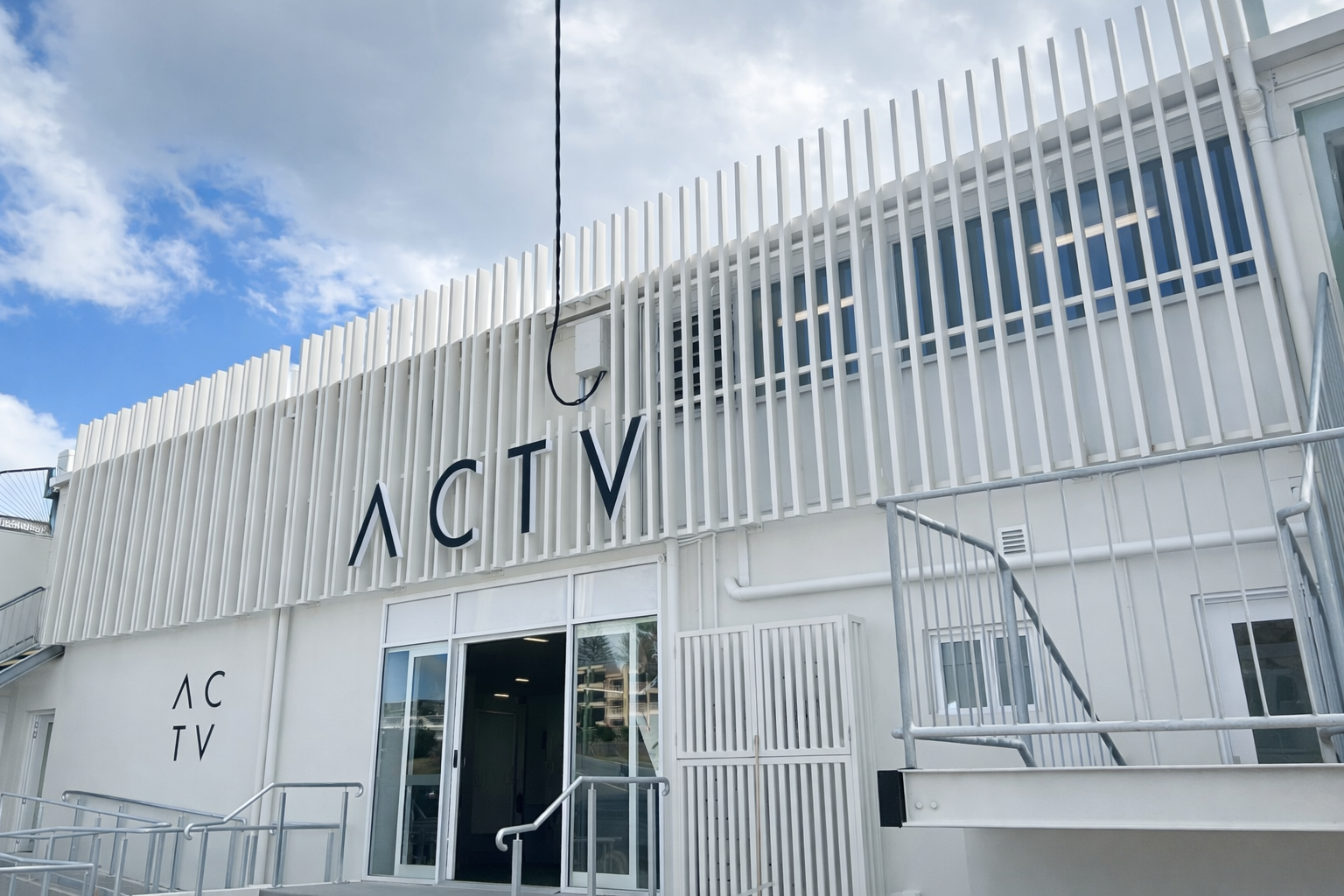 White storefront with “ACTV” signage and a glass entrance under a blue sky.