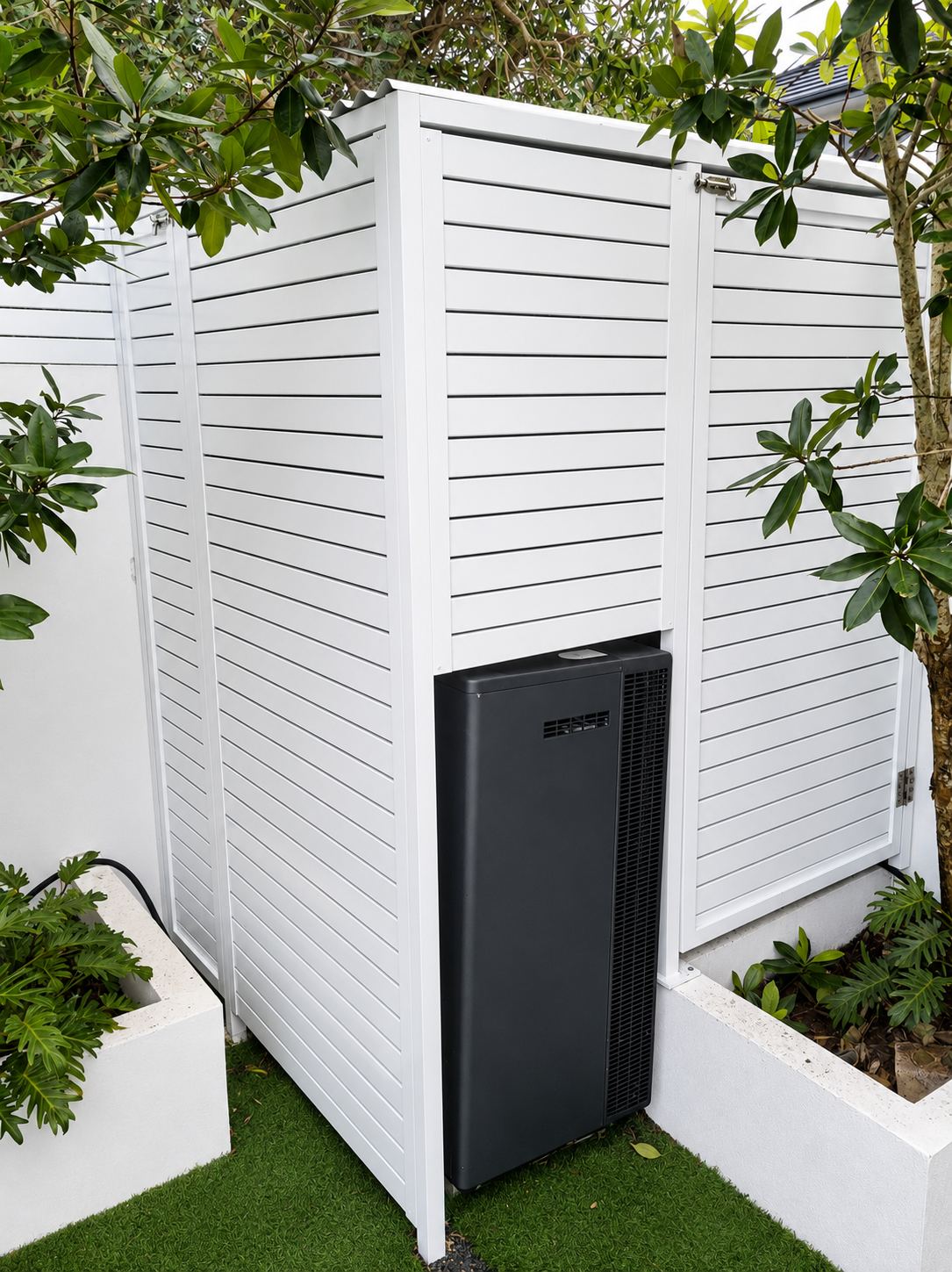 White slatted outdoor enclosure with a black utility unit, framed by greenery and planter boxes