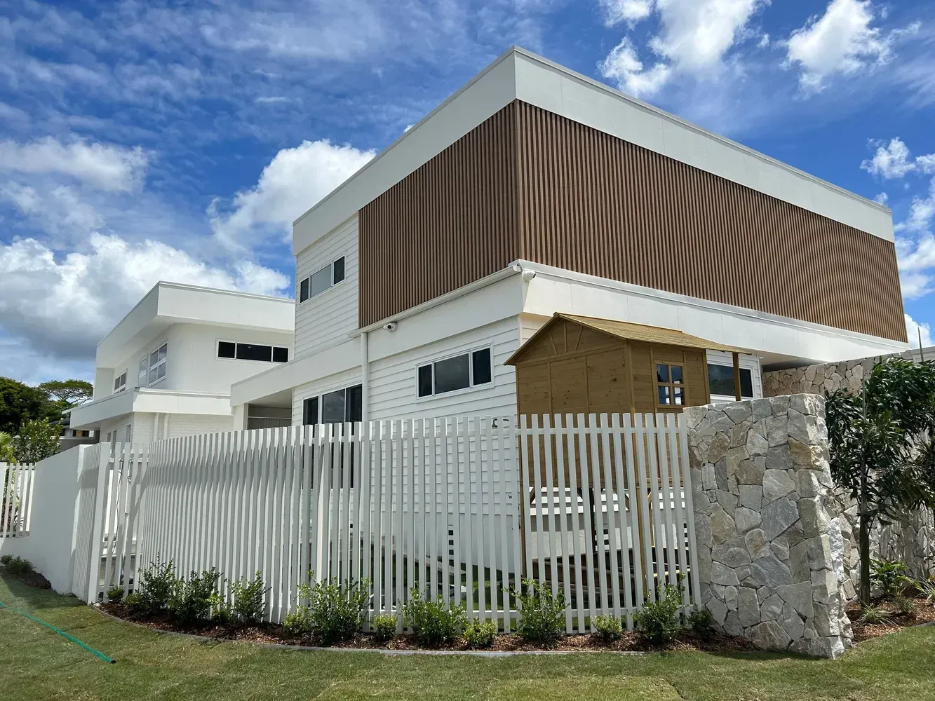 Modern Two-story House With Wood Slats, White Fence, And Stone Wall — Frontline Fences in Tweed Heads South, NSW