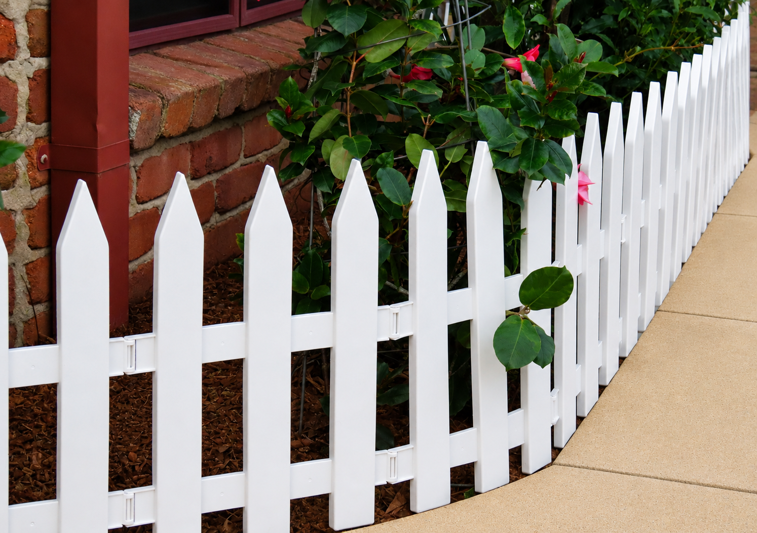 White Picket Fence Beside a Brick Wall and Sidewalk, With Green Vines Growing Through It — Frontline Fences in Tweed Heads South, NSW