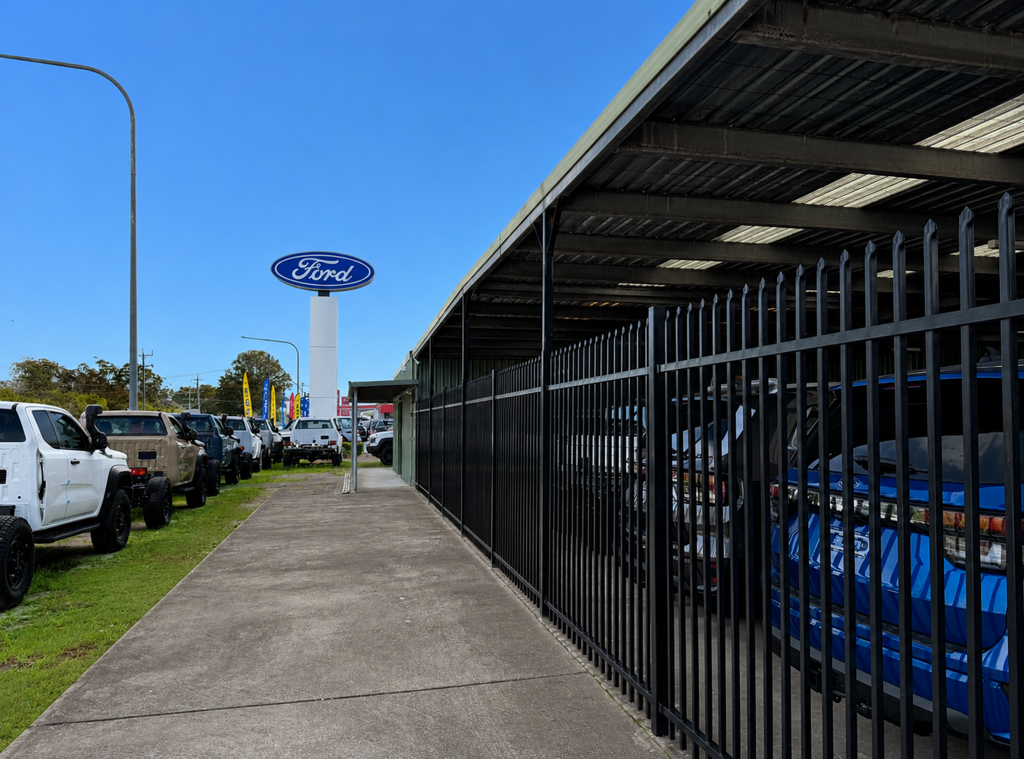 Car Lot with Parked Vehicles, a Ford Sign, and A Blue Car Behind a Black Metal Fence Under a Covered Awning — Frontline Fences in Tweed Heads South, NSW