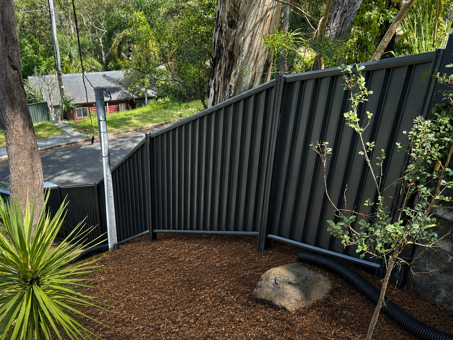 Curved Black Metal Fence Beside a Gravel Yard With Trees and a Small House in the Background — Frontline Fences in Tweed Heads South, NSW