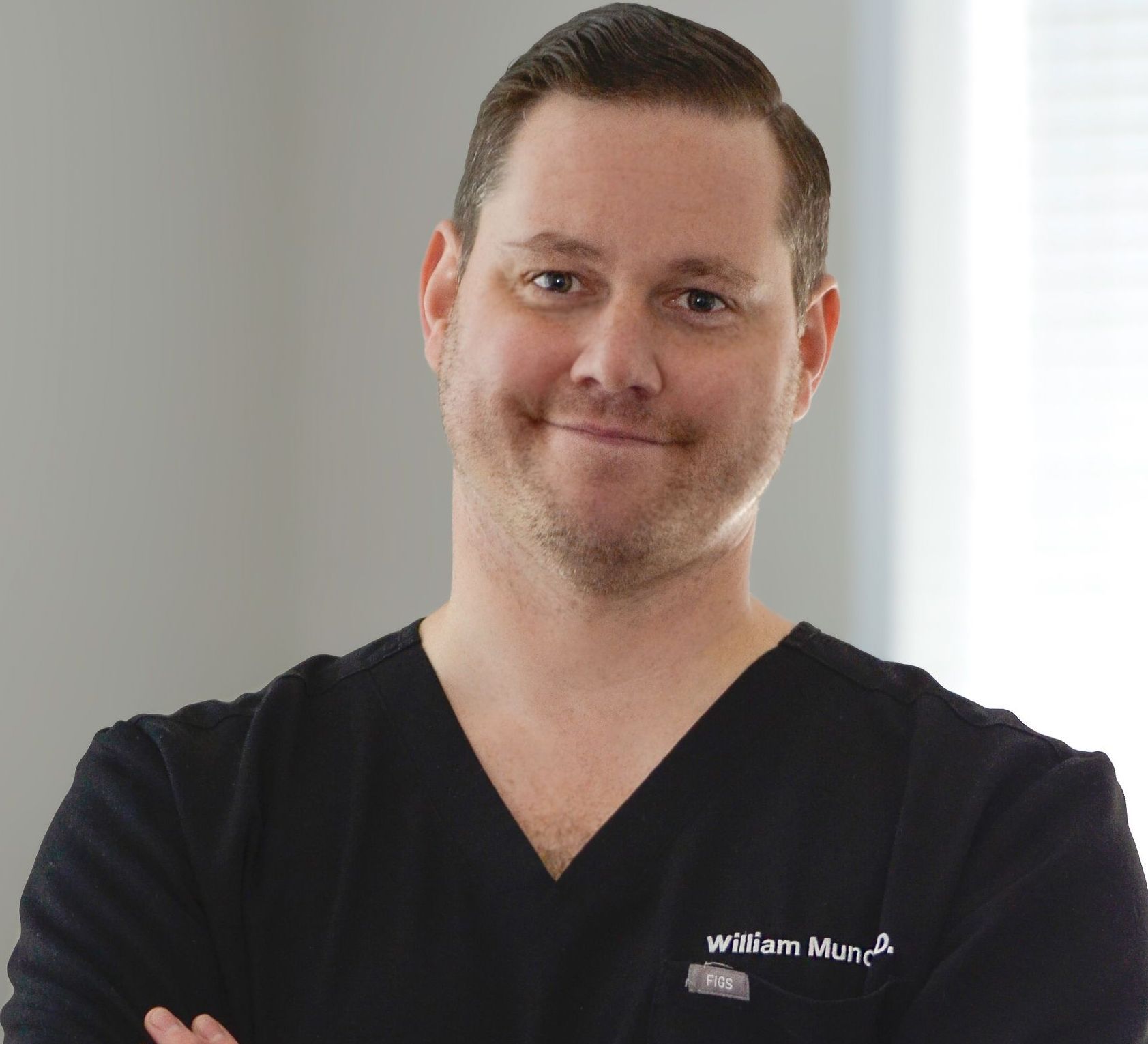 A man wearing a black scrub top with the name william mun on it