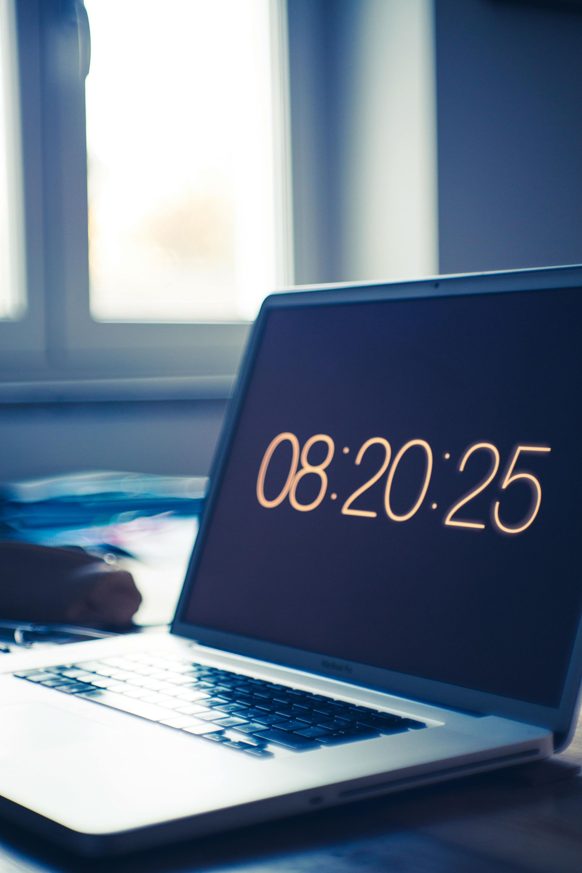 Laptop screen displaying time 08:20:25, placed in front of a window.