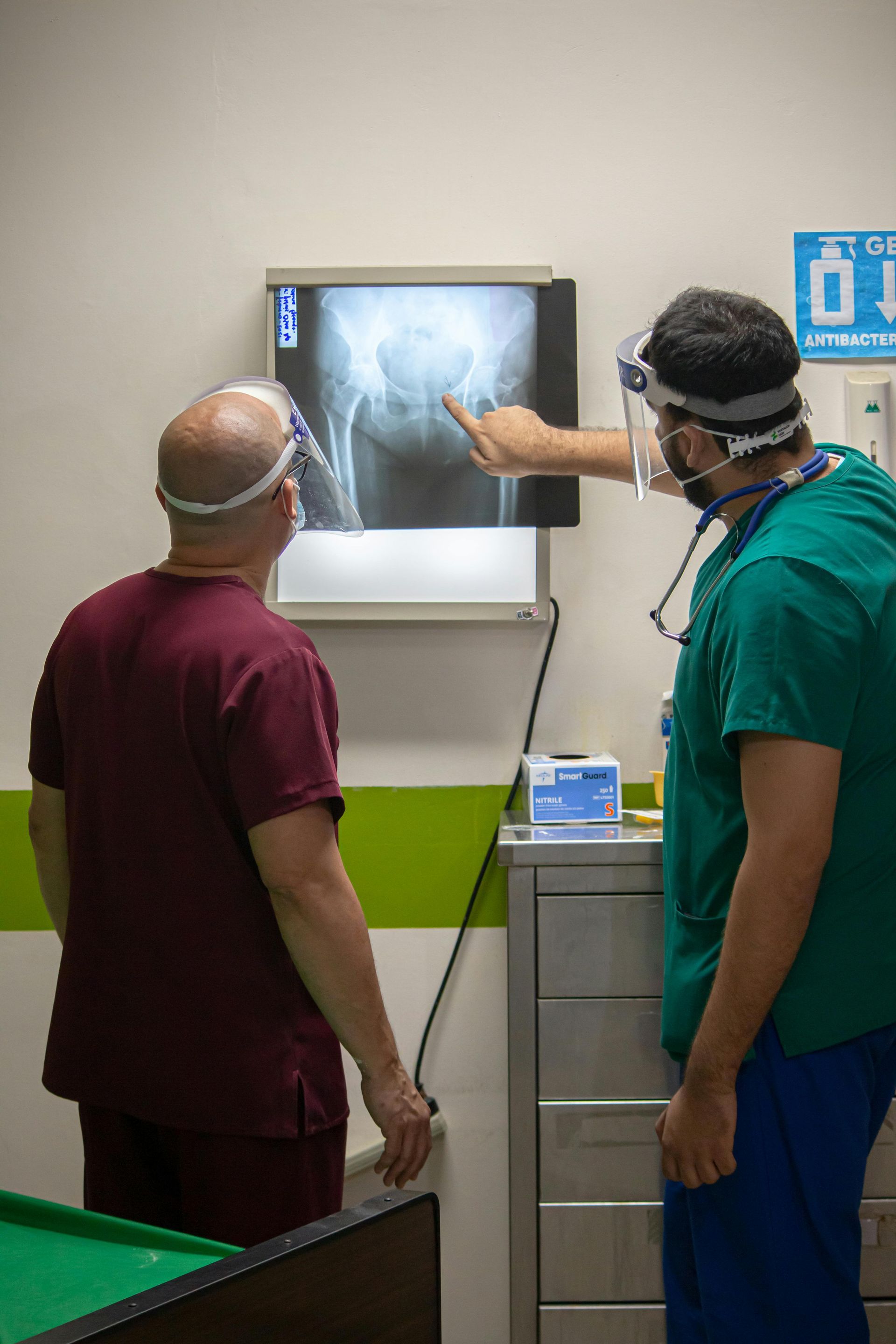Two people in scrubs look at an X-ray on a light box. One points to the image.