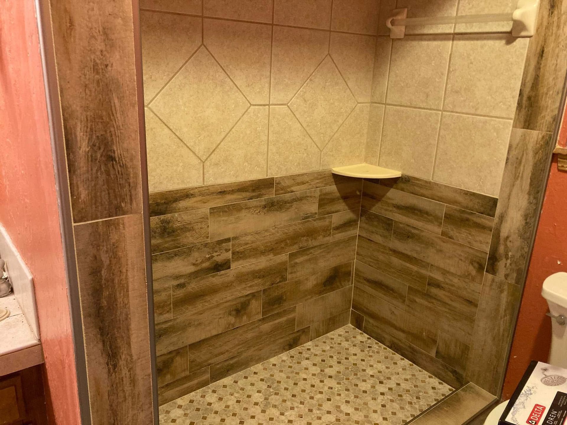Shower stall with wood-look tile on the lower half and diamond-patterned tile above, with a built-in shelf.