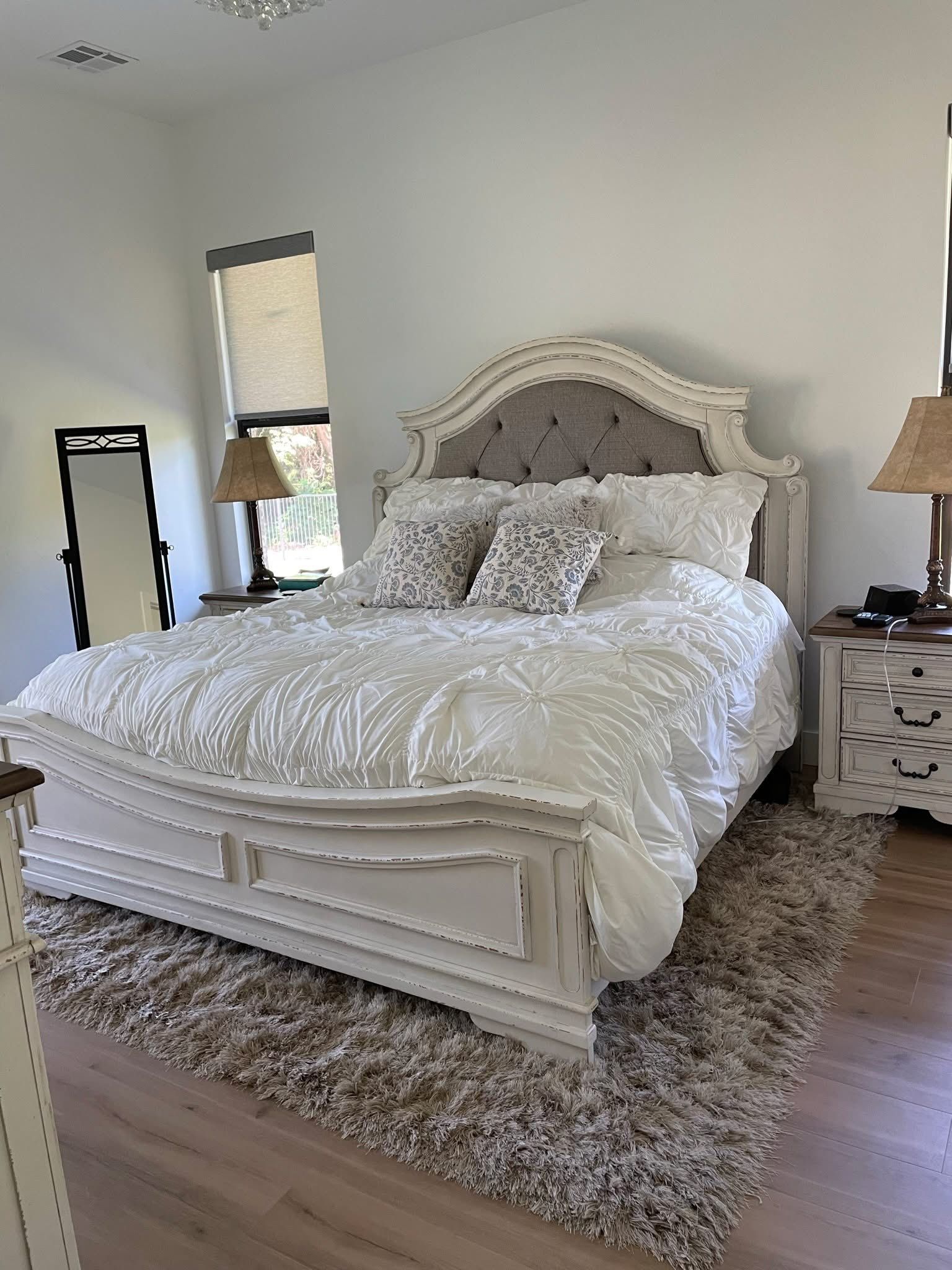 A bedroom featuring a white bed with decorative headboard, white bedding, and a plush rug. 