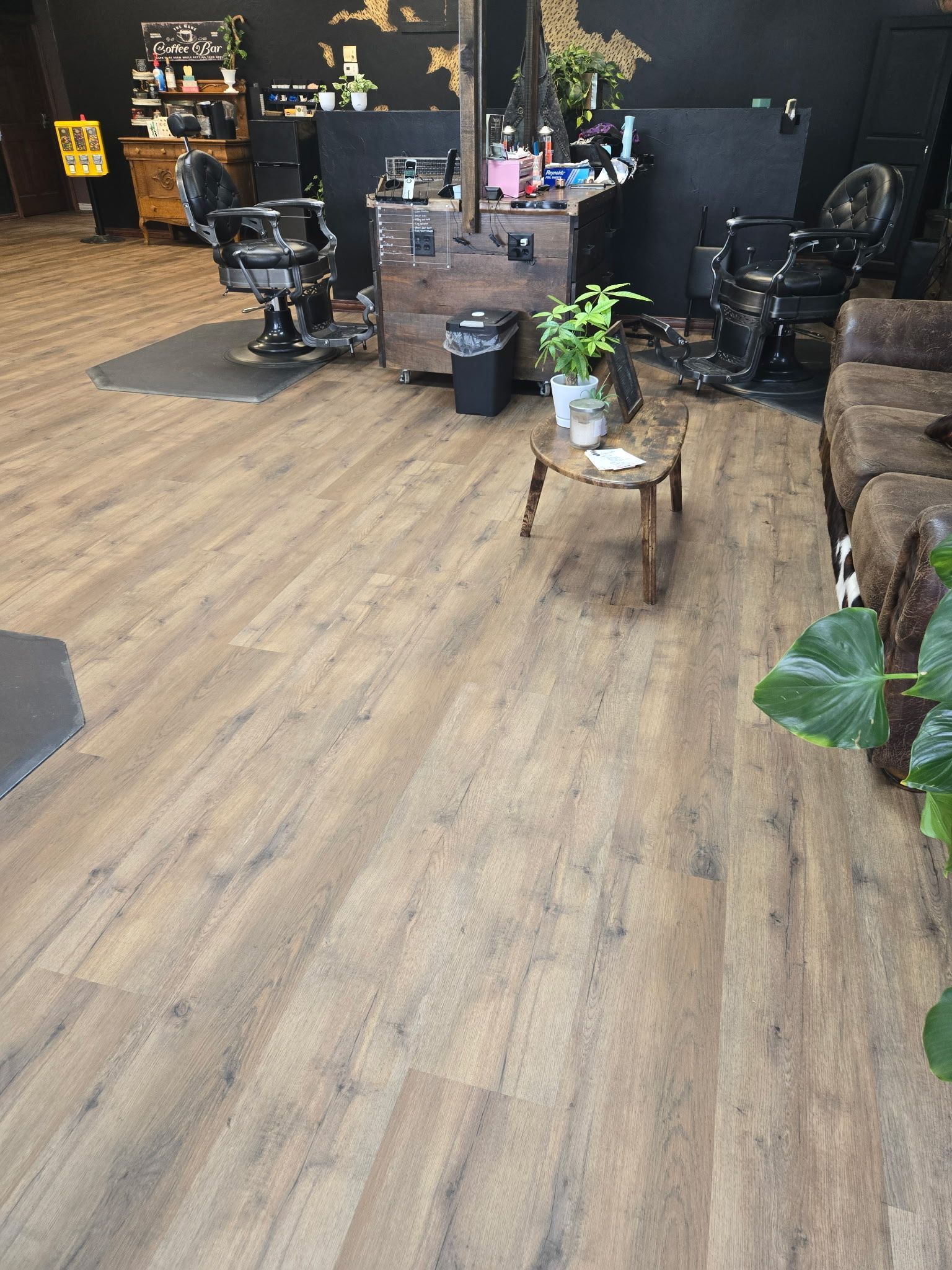 Barber shop interior with wooden floor, black chairs, and a coffee table with plants.