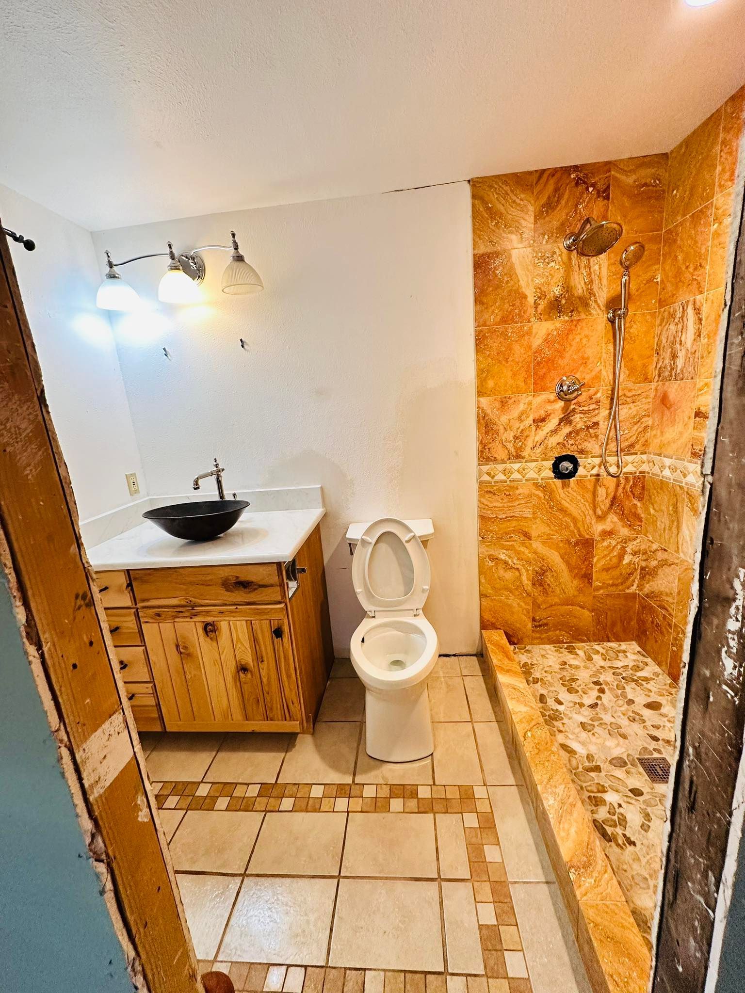 Bathroom with rustic wood vanity, black bowl sink, tiled shower, and toilet.