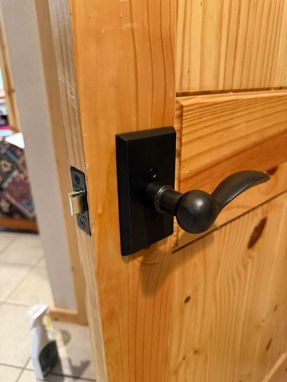 Black door handle on a light-colored wooden door. The handle is lever-style and rectangular.