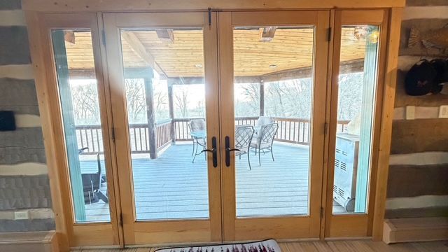 Glass doors open onto a porch with chairs and a view of trees.