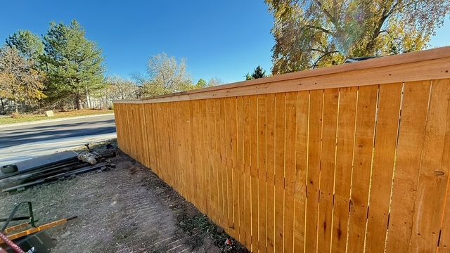Wooden privacy fence along a road, clear blue sky overhead.